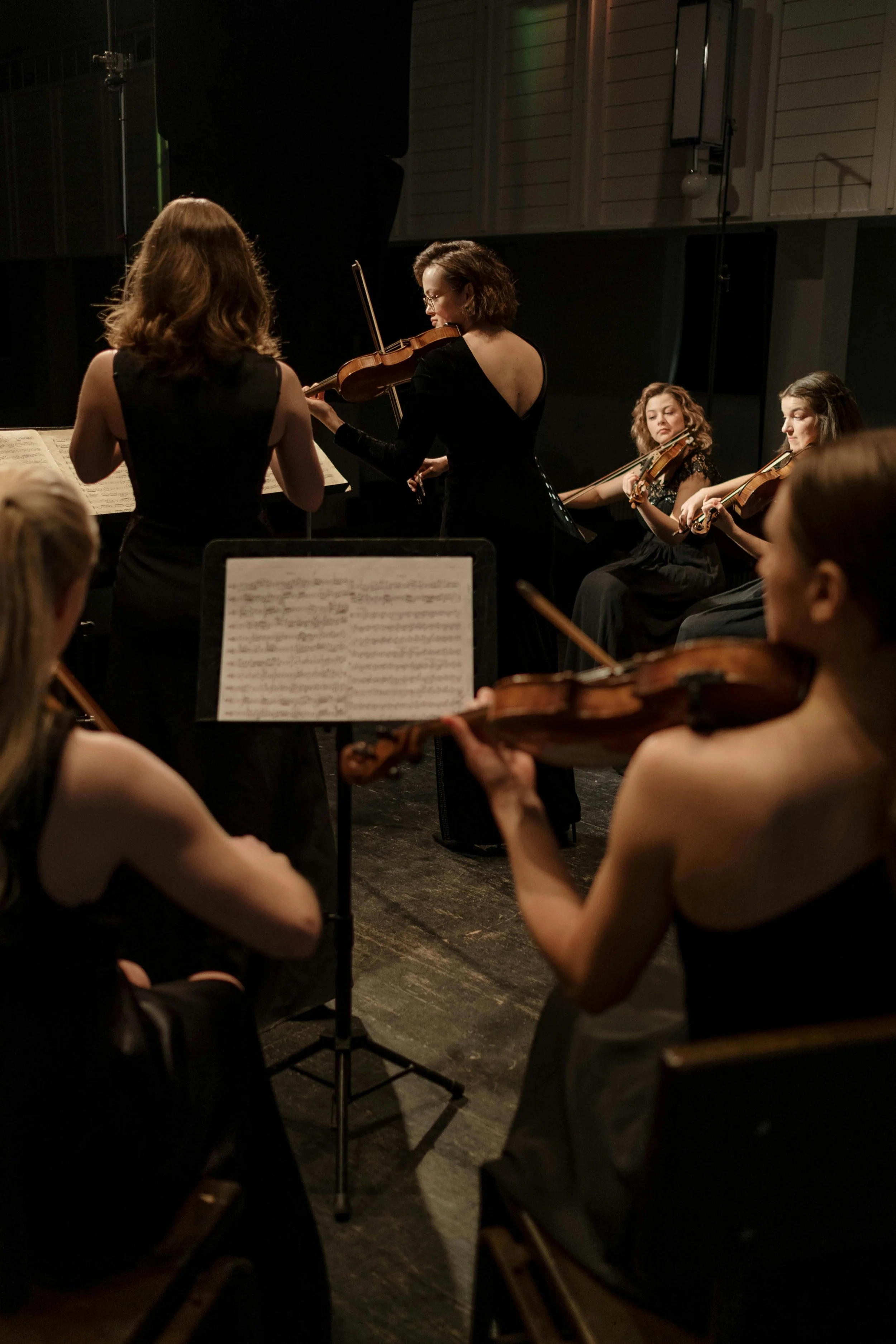Orchestra of women playing violins during a concert, with sheet music on a stand in the foreground.