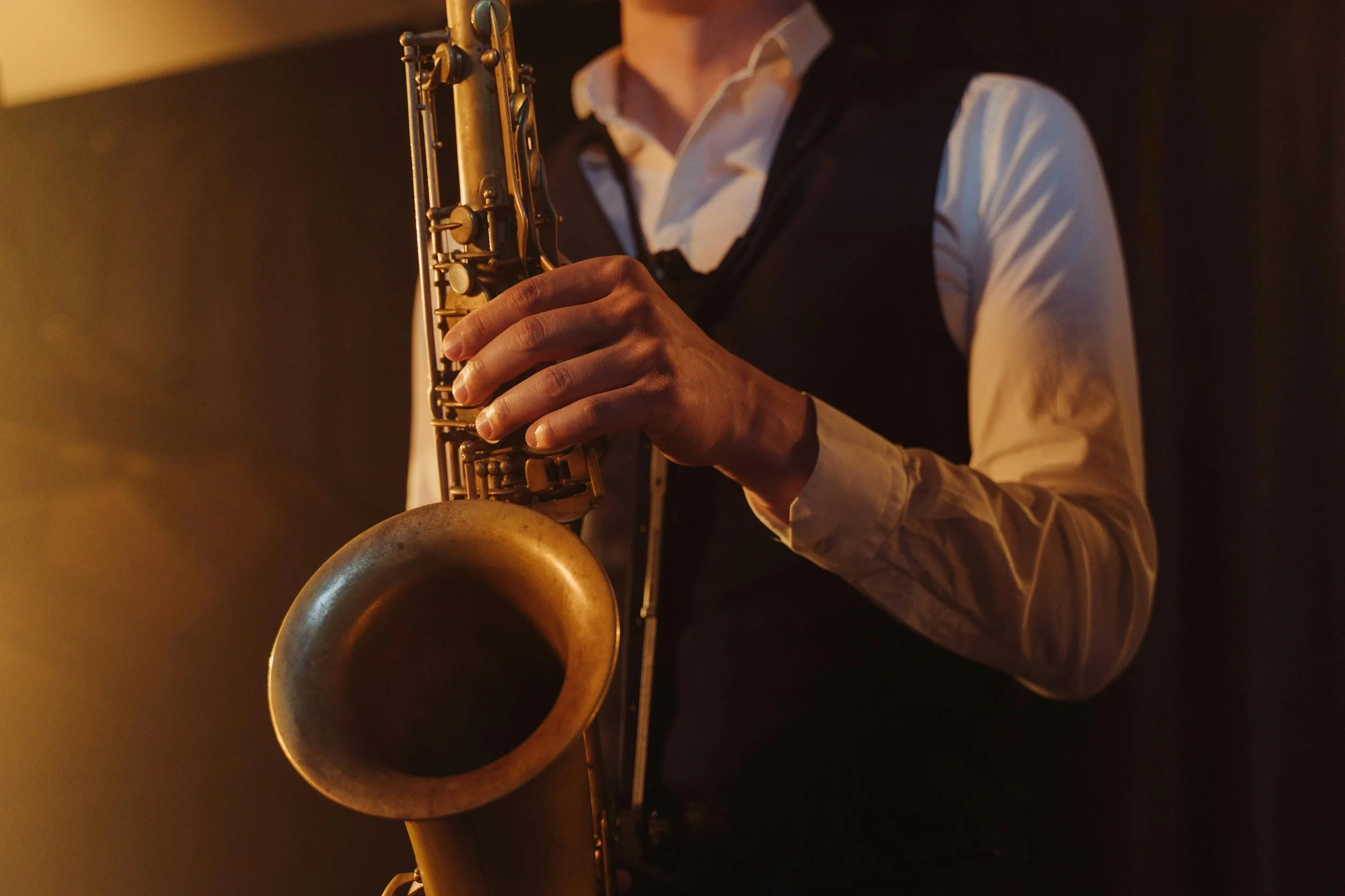 A person wearing a white shirt and black vest playing a saxophone.