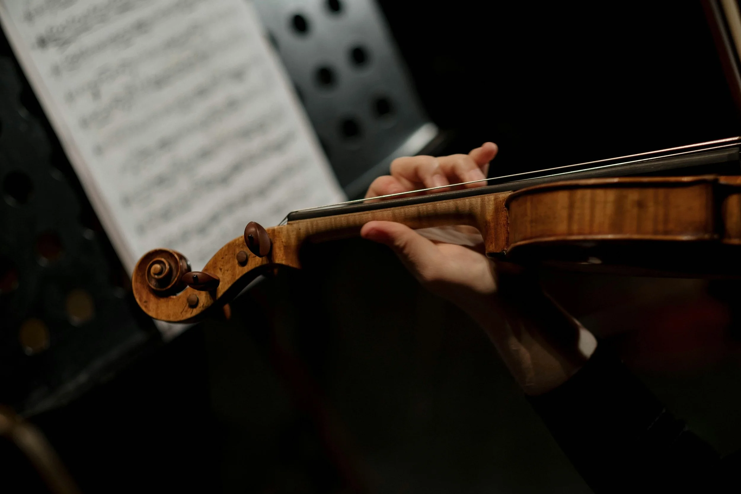 A person holding a wooden violin with sheet music and a music stand in the background.