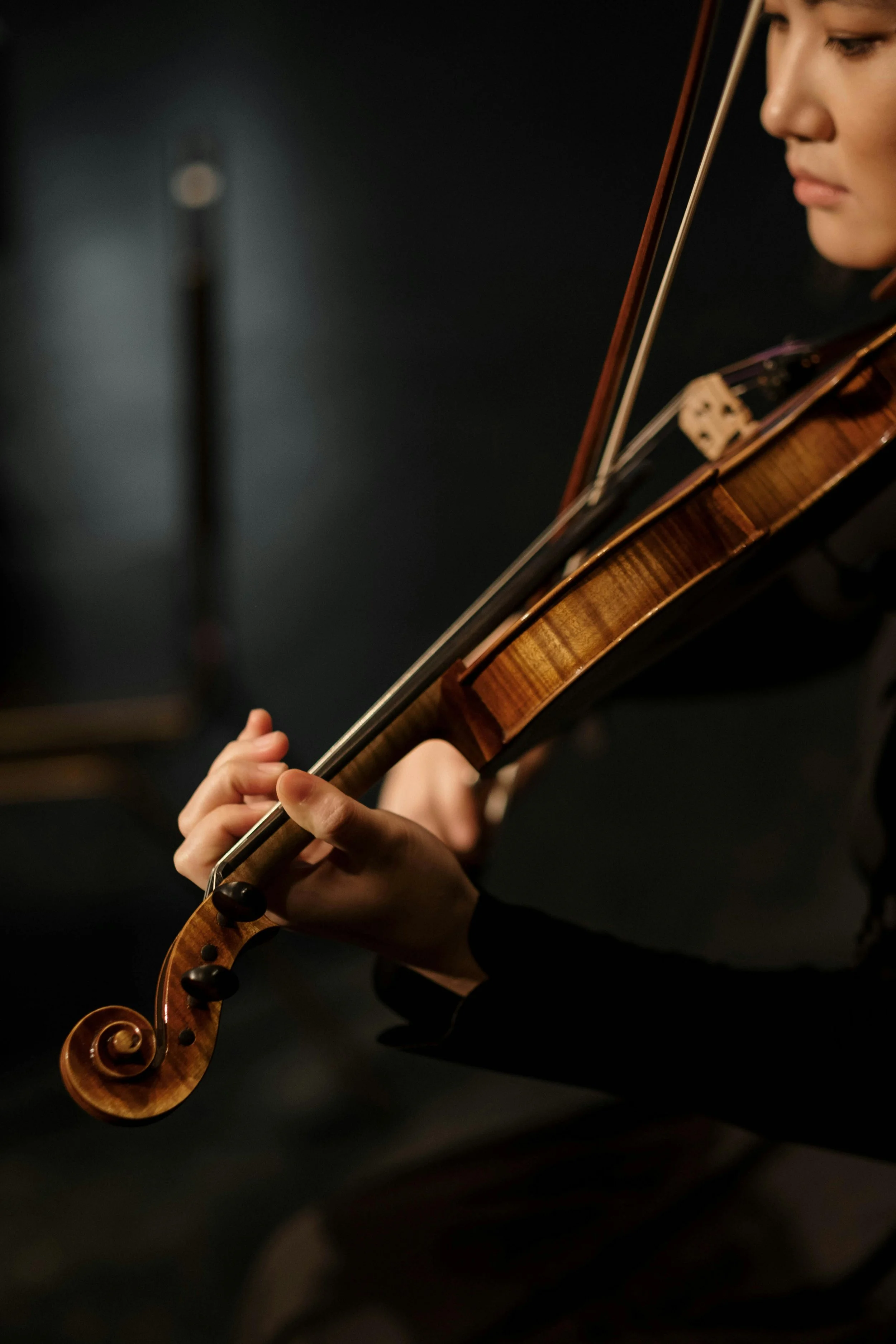 Close-up of a person playing a violin, focusing on their hand on the fingerboard and the scroll of the violin.