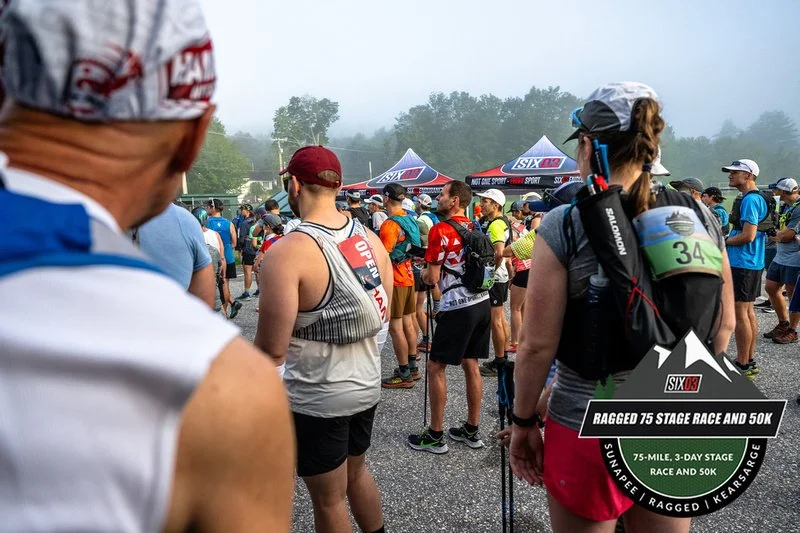 Participants gathered at the starting line of the Ragged 75 Stage Race and 50K, an endurance race featuring a 75-mile, 3-day stage race and a 50K race, with tents in the background and people dressed in athletic gear.