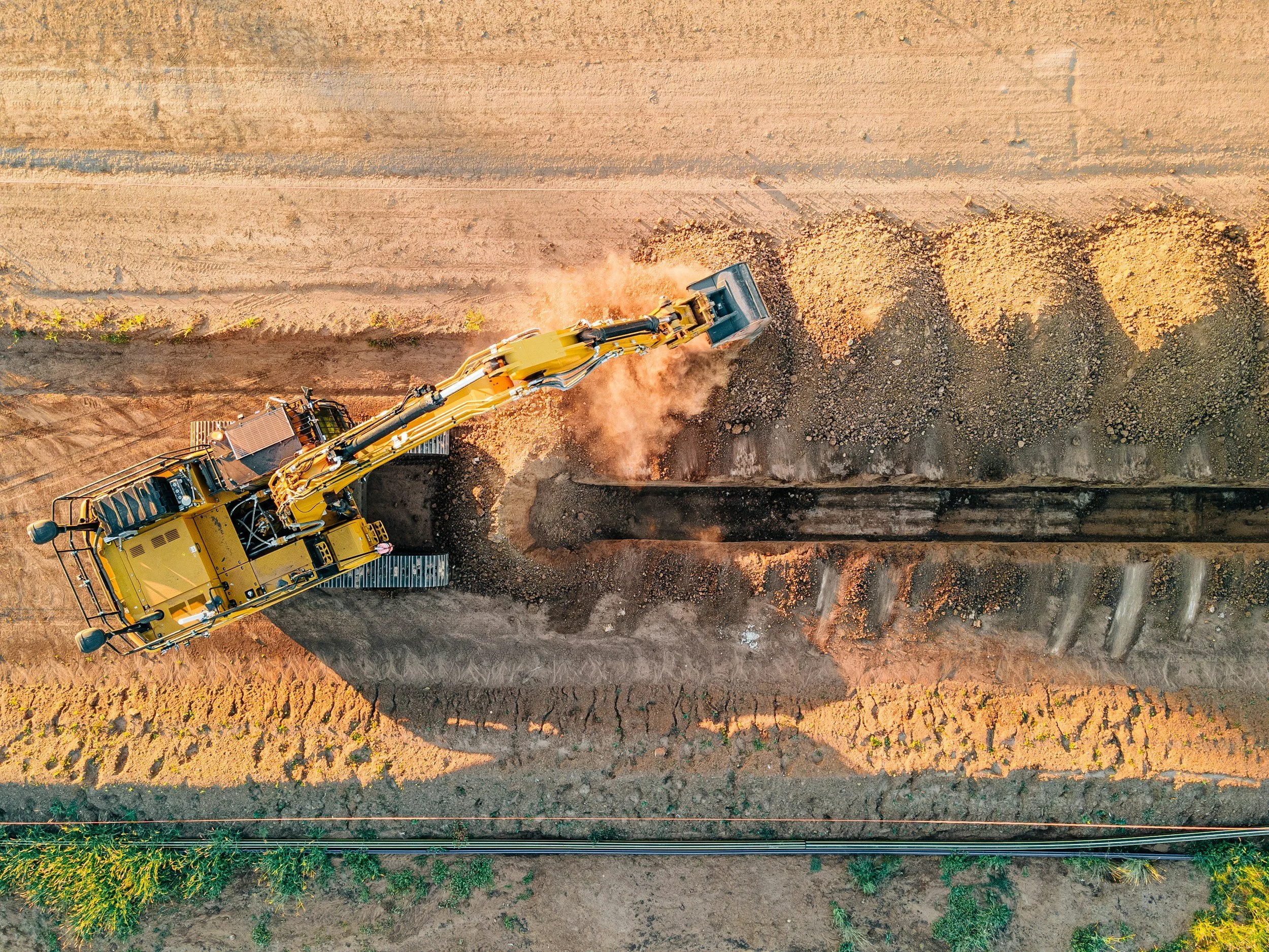 Vogelperspektive auf eine große gelbe Bagger beim Aushub auf einer Baustelle, mit Erde und Steinen.