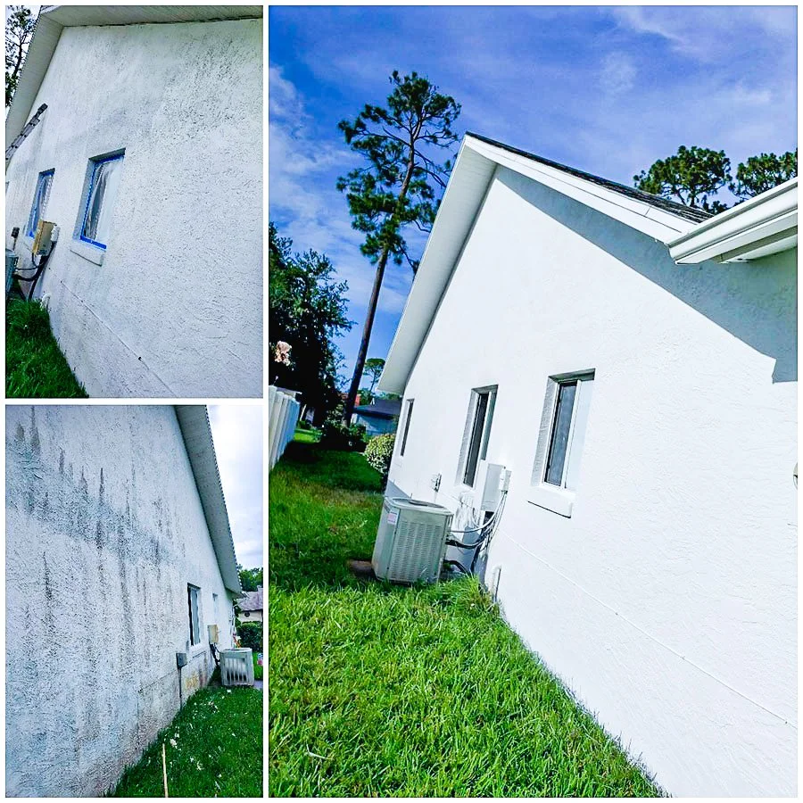 Side view of a white house with two small windows, an air conditioning unit outside, and lush green grass under a blue sky with trees.