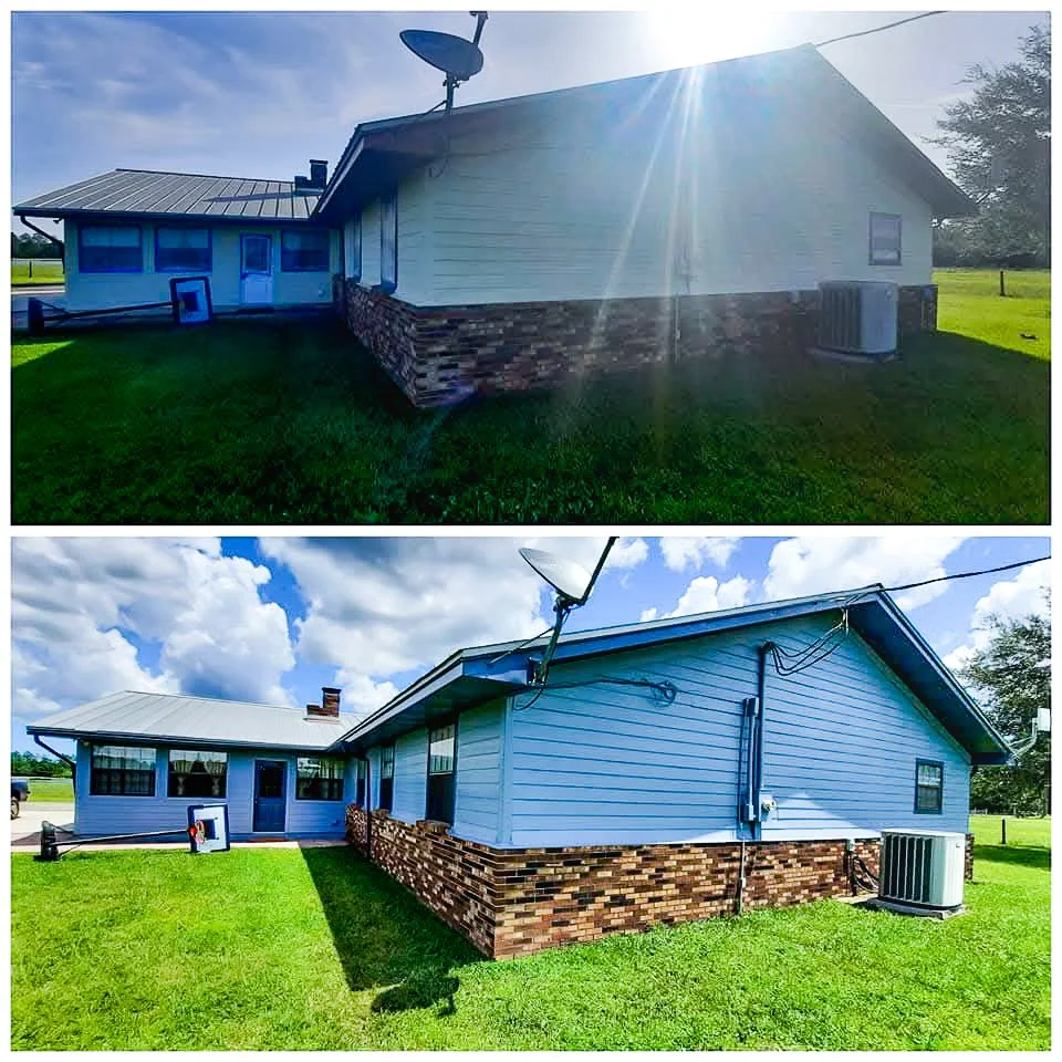 Side view of a blue house with a brick foundation, satellite dish on the roof, and a backyard with green grass and a clear sky.