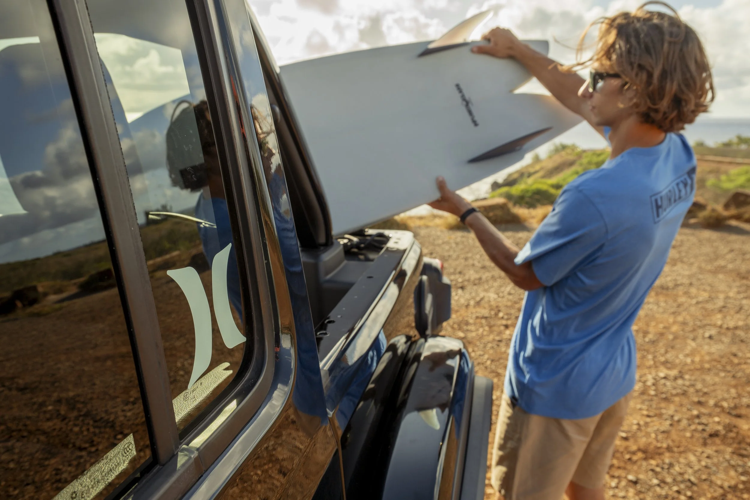 Man putting a surfboard in the trunk of his car with a Hurley decal sticker