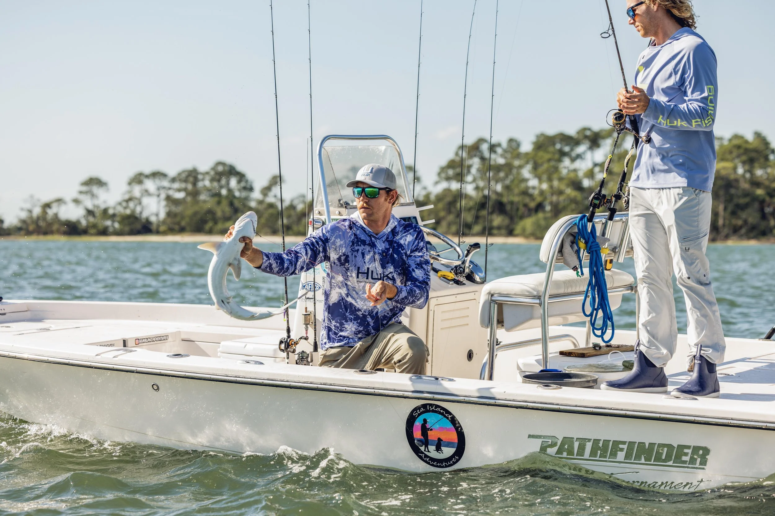 Two people wearing Huk sunglasses fishing on a boat