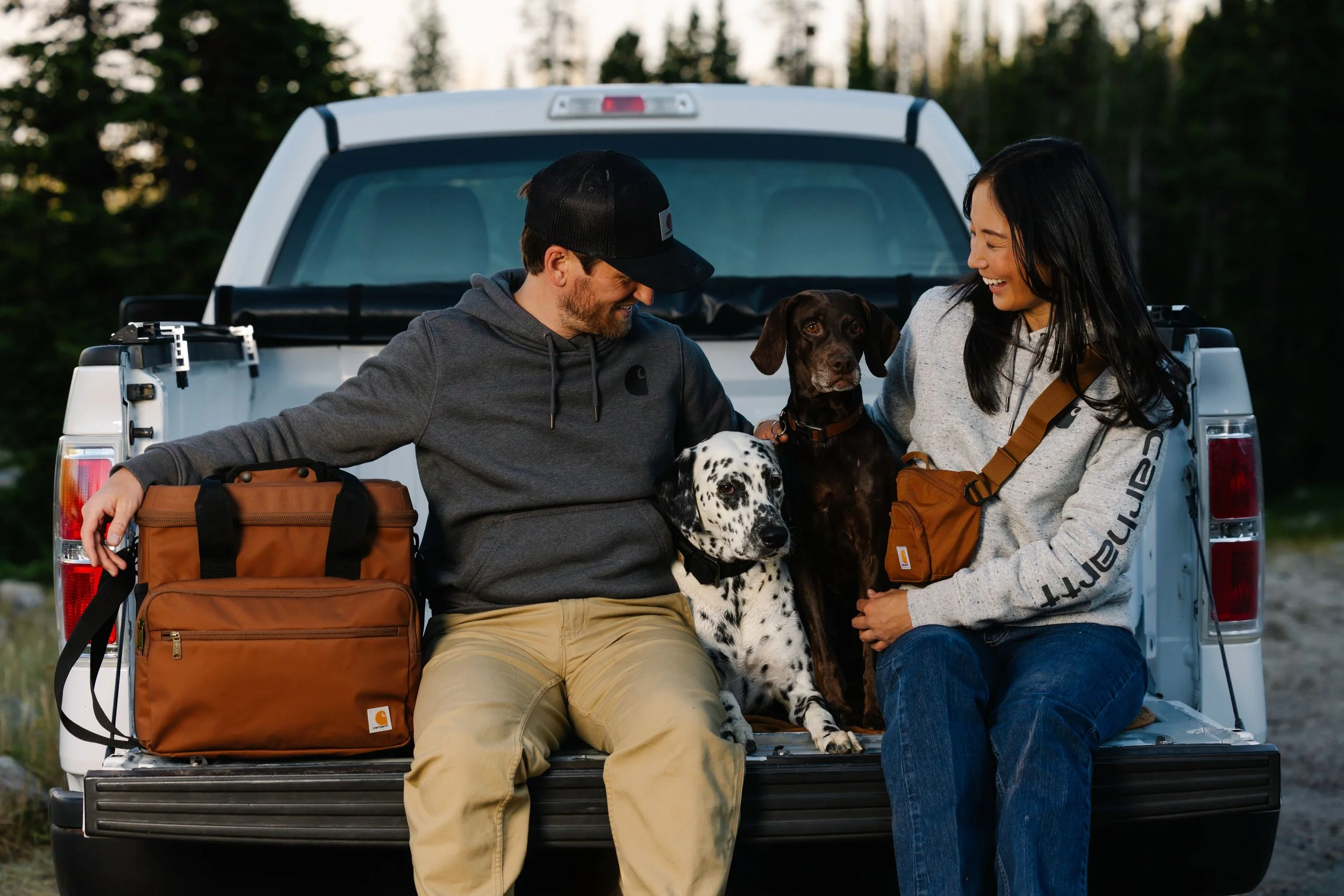 A man, woman, and two dogs in the back of a truck with Carhartt bags and sweatshirts