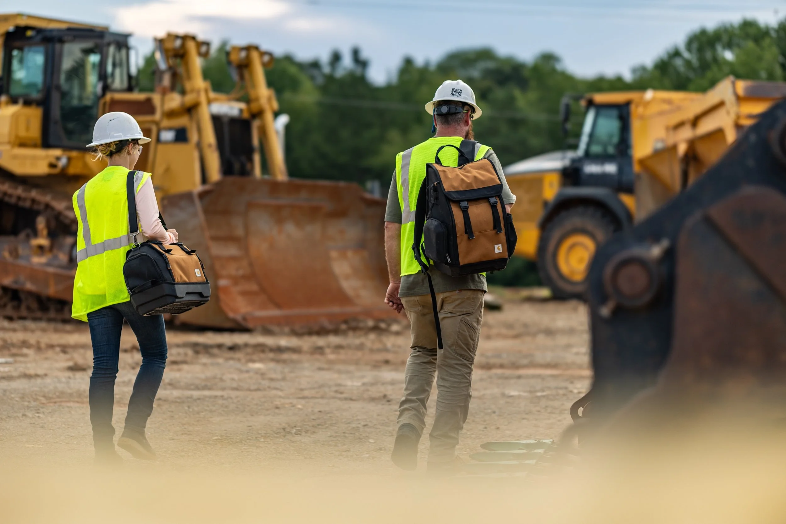 Two construction workers walking down the site with Carhartt bags