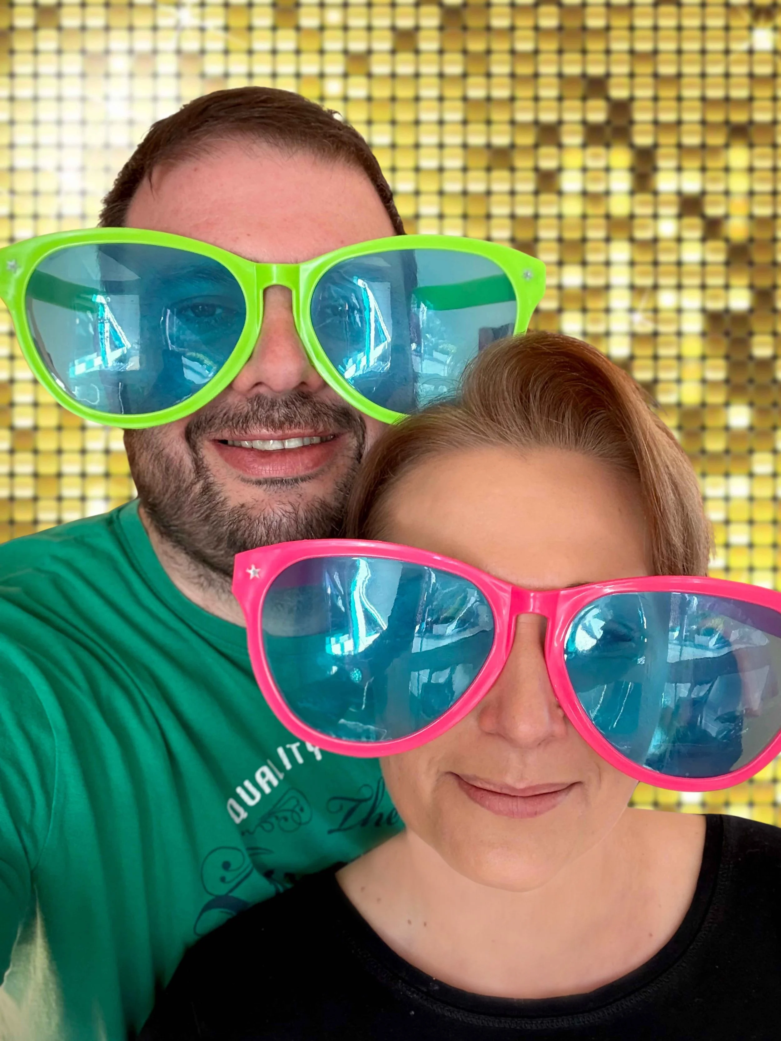 Das Fotobox Bad Driburg Team, mit bunter Sonnenbrillen und posieren vor einem goldenen, pixelartigen Hintergrund.