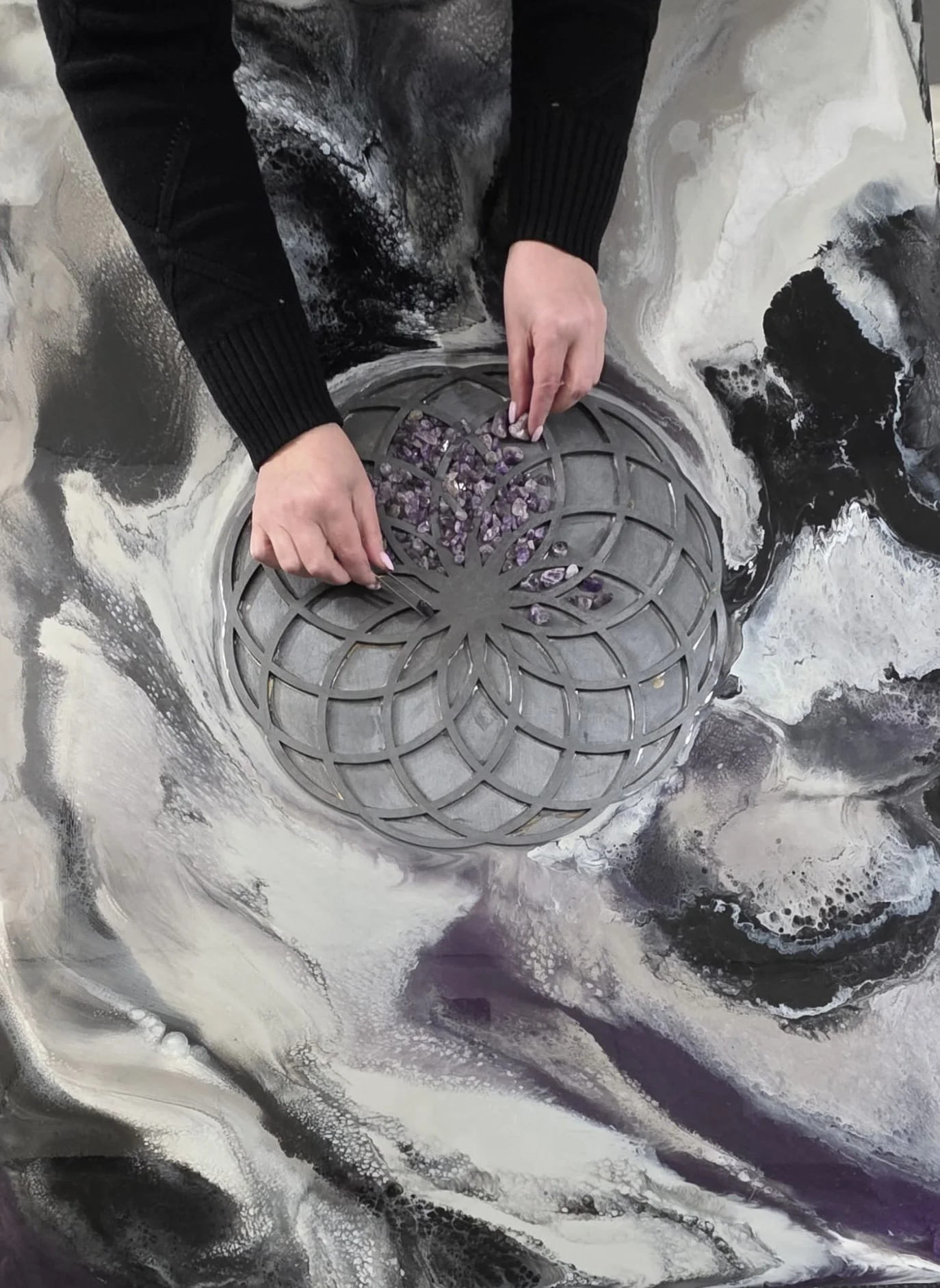 Tatyana Y. Kravchenko is placing purple gemstones onto a metal grate with a swirling black, white, and gray pattern on the ground.