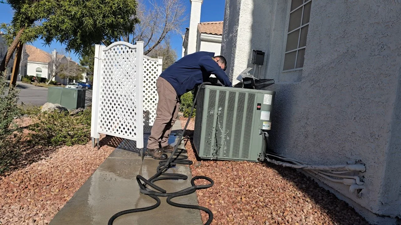 A technician servicing an outdoor air conditioning unit outside a house on a sunny day.