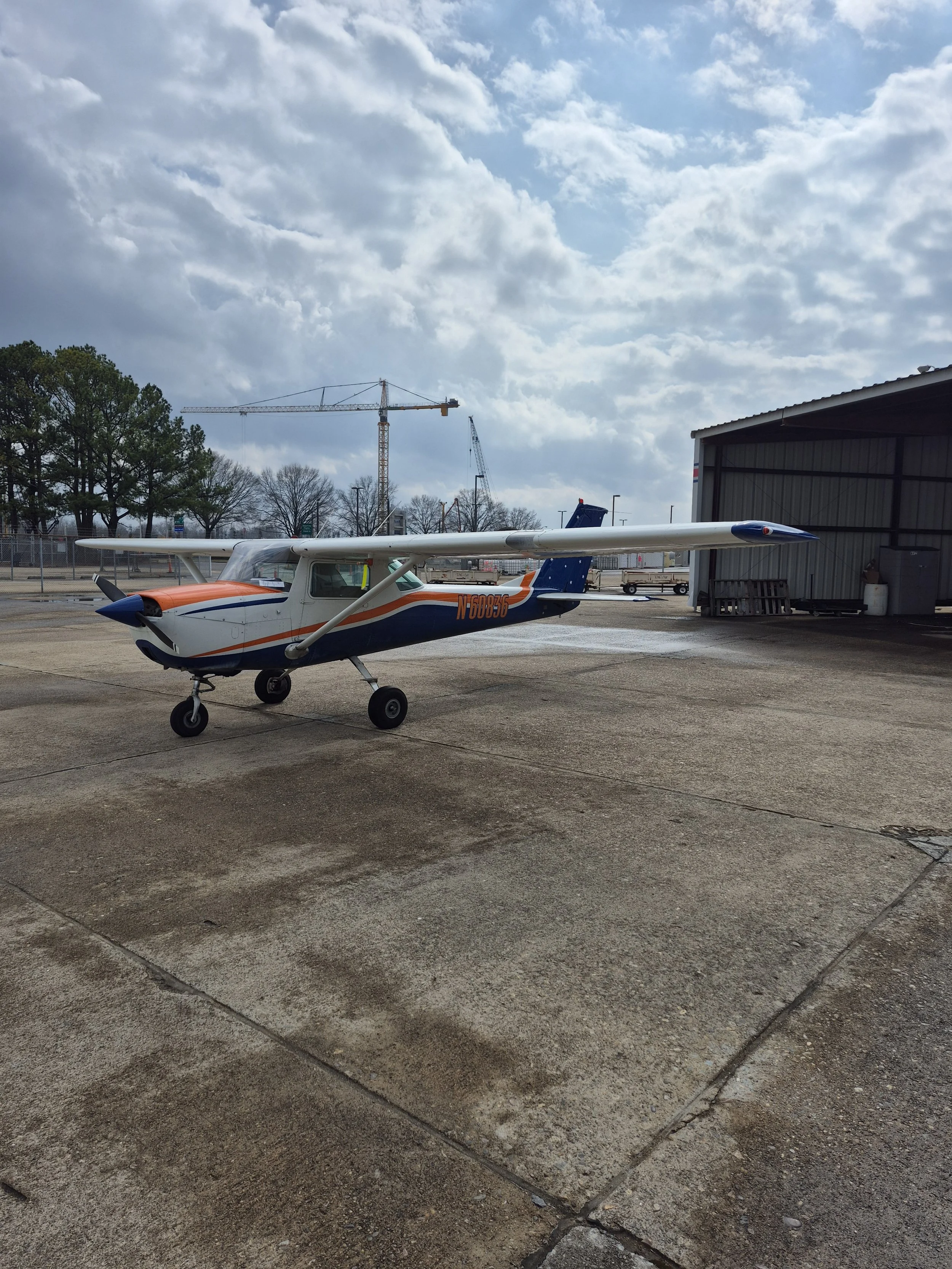 A Cessna 150, painted in white, blue, and orange, parked on the ramp at McGhee Tyson Airport.