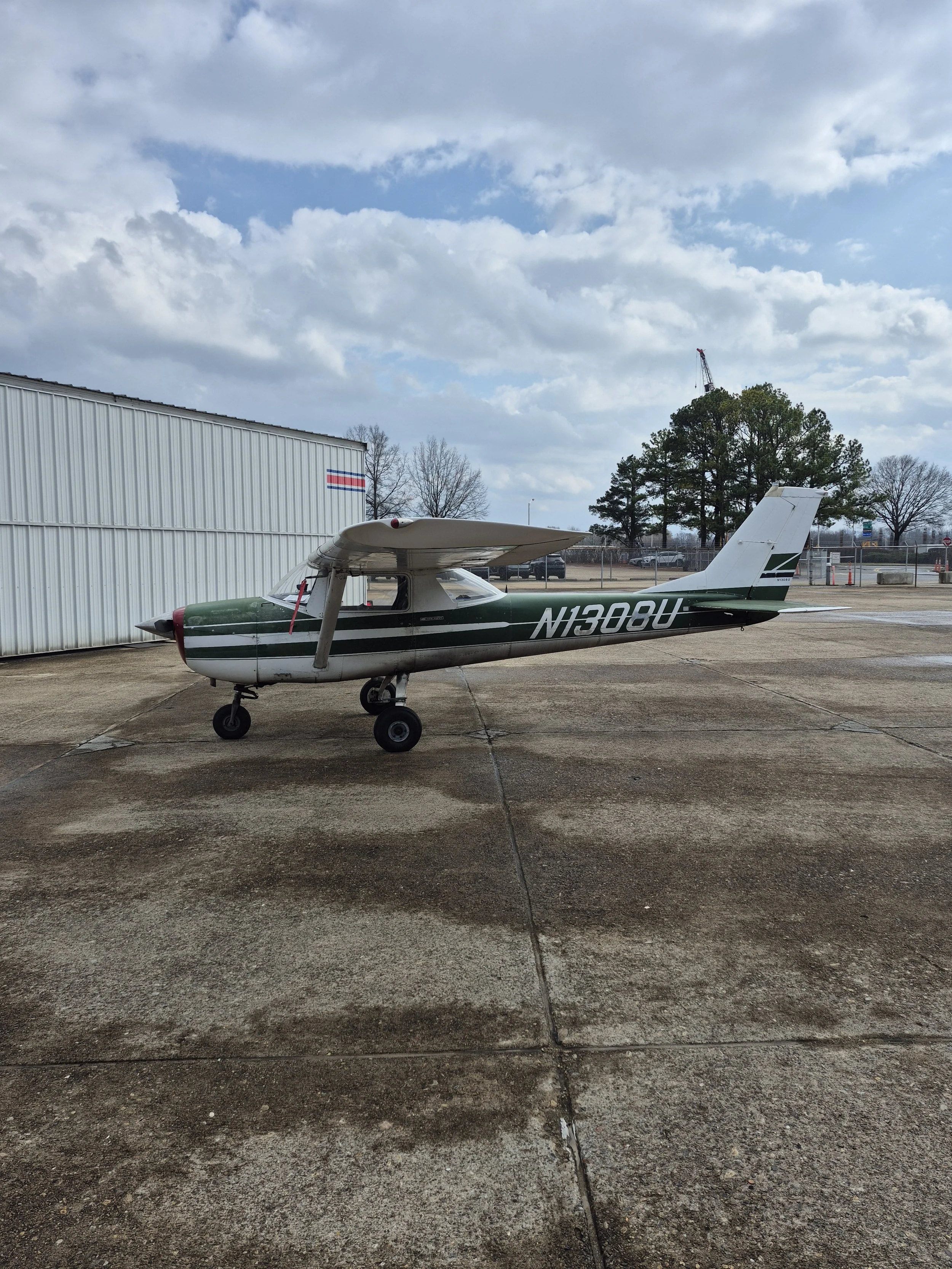 Small vintage airplane painted green and white with the registration number N1308U parked on a concrete tarmac.