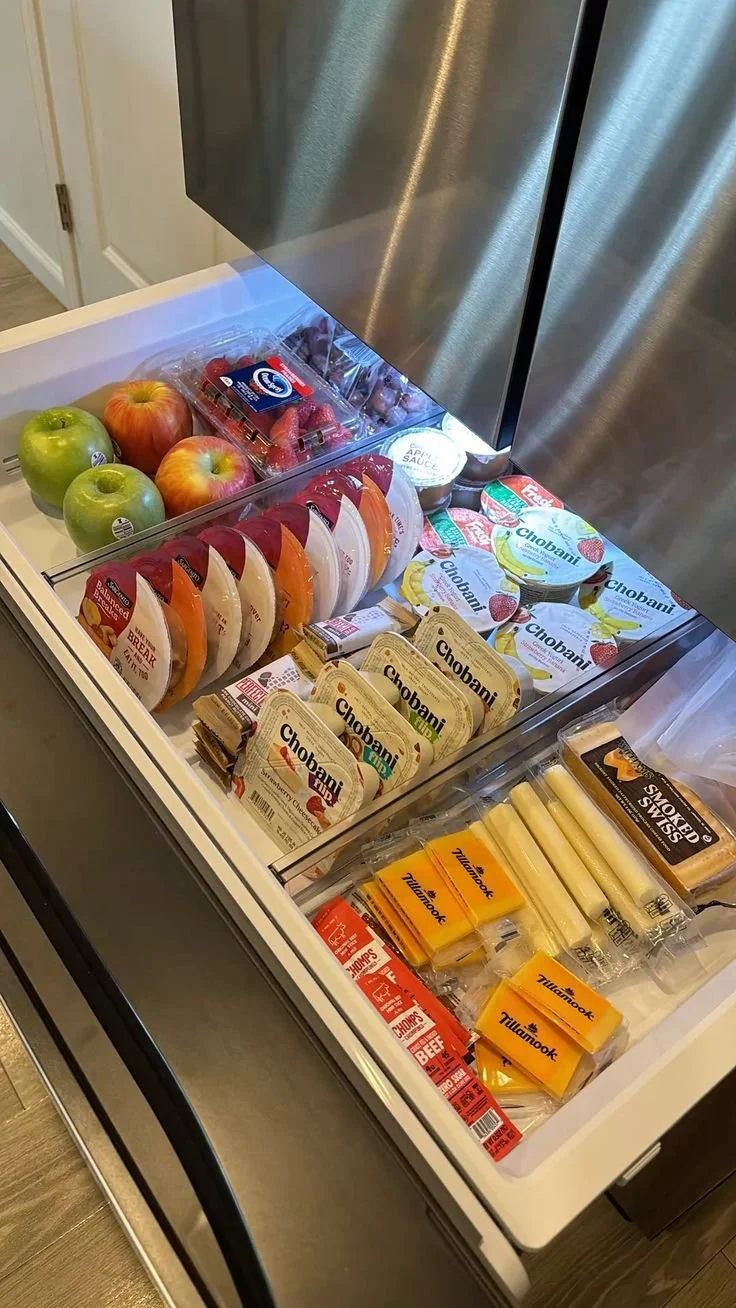 Open freezer drawer with apples, strawberries, cheeses, and deli meats inside.