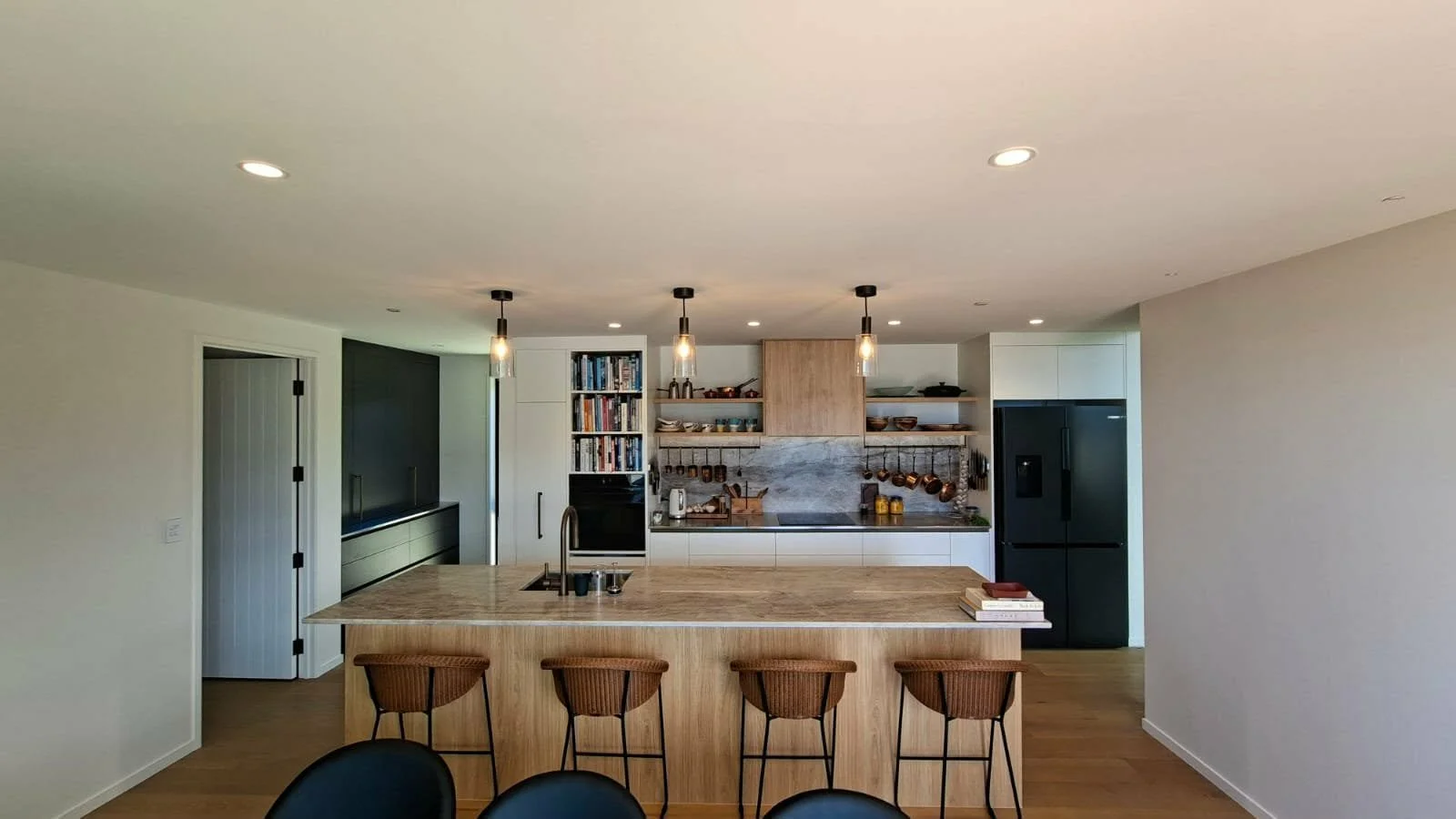 Modern kitchen with a large island, black refrigerator, open shelving, and pendant lighting.