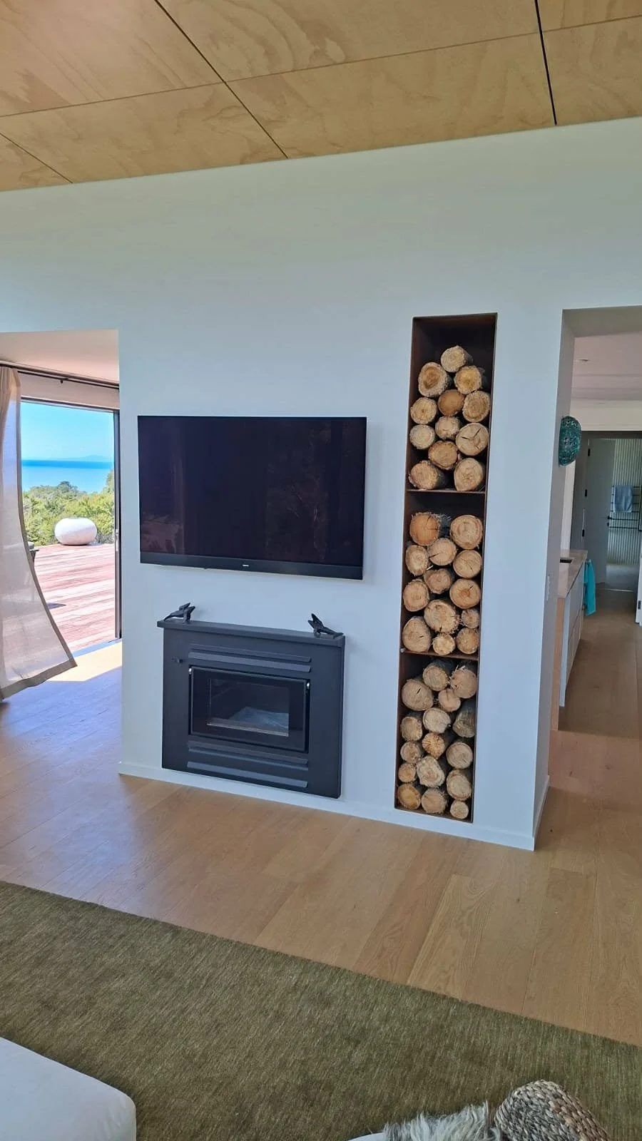 Living room with a wall-mounted TV above a black fireplace and a tall, narrow wood storage nook filled with firewood logs.