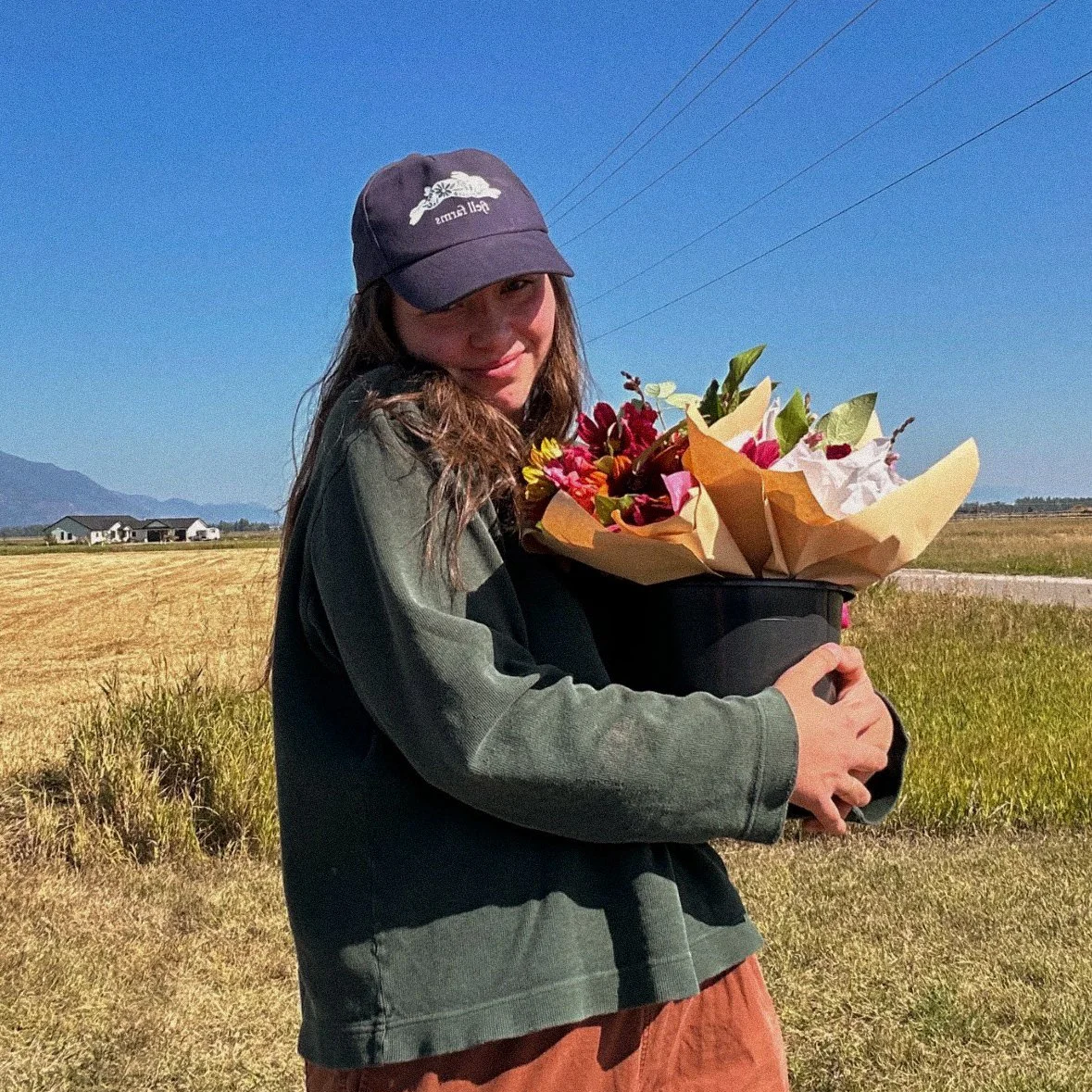 Eva, owner of Fjell Farms, holding a fresh-cut market wrap bouquet with Montana mountains in the background