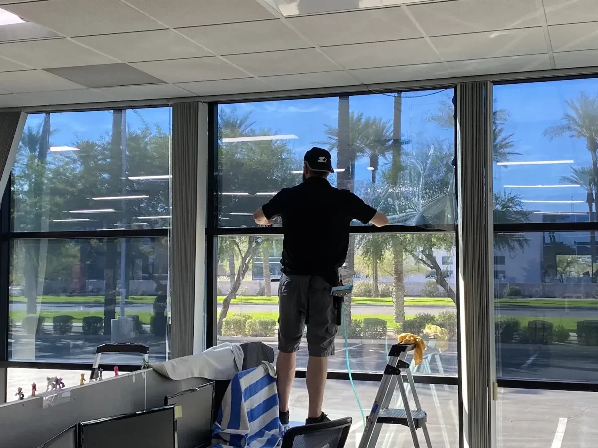 A person cleaning a large window with a squeegee inside a building with a view of palm trees outside.