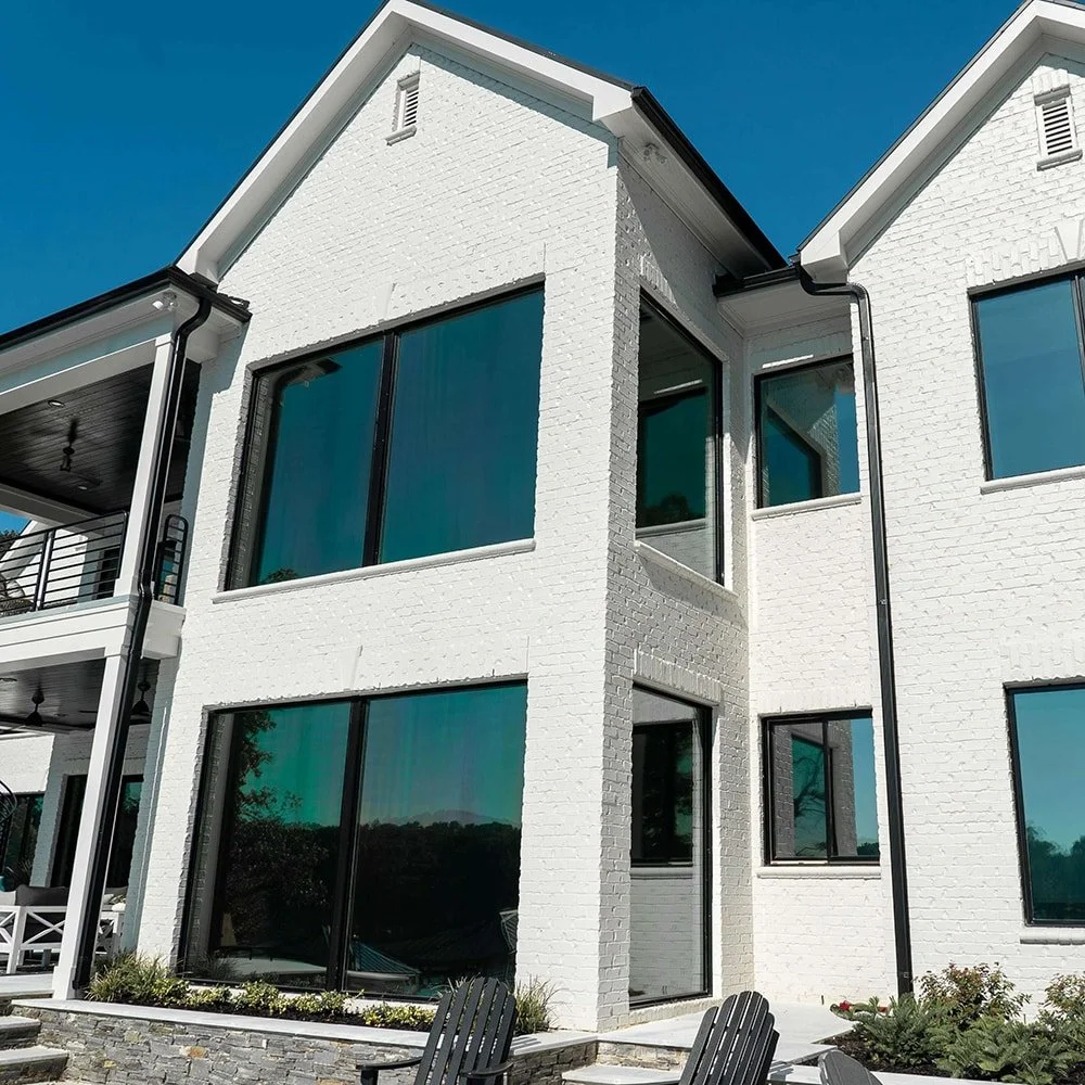 A modern white brick house with large glass windows under a clear blue sky.