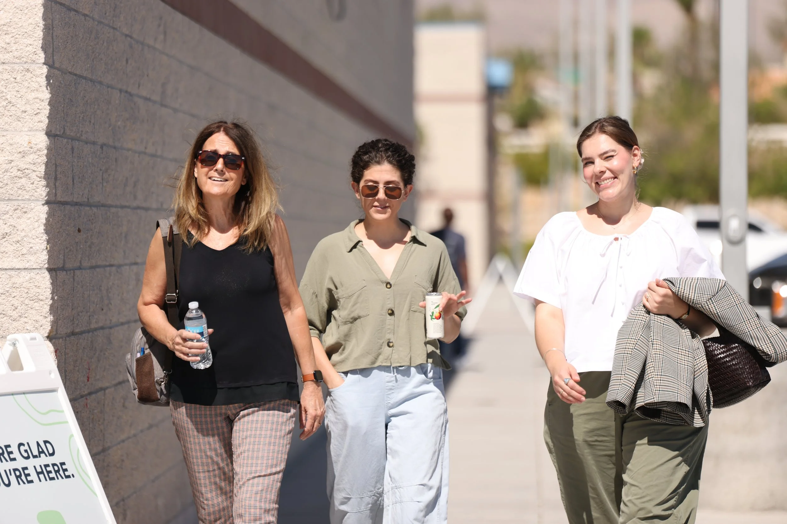 Three women walking outside on a sunny day, smiling and holding drinks, entering the church service which is held at a middle school campus.