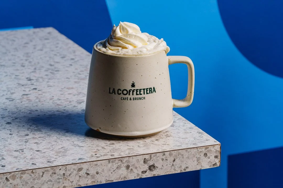 Taza de cerámica con leche o café y crema batida, en un ambiente con fondo azul.