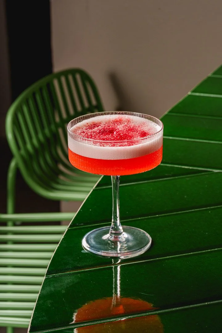 Cóctel rojo en copa de vidrio en mesa verde, fondo con silla verde