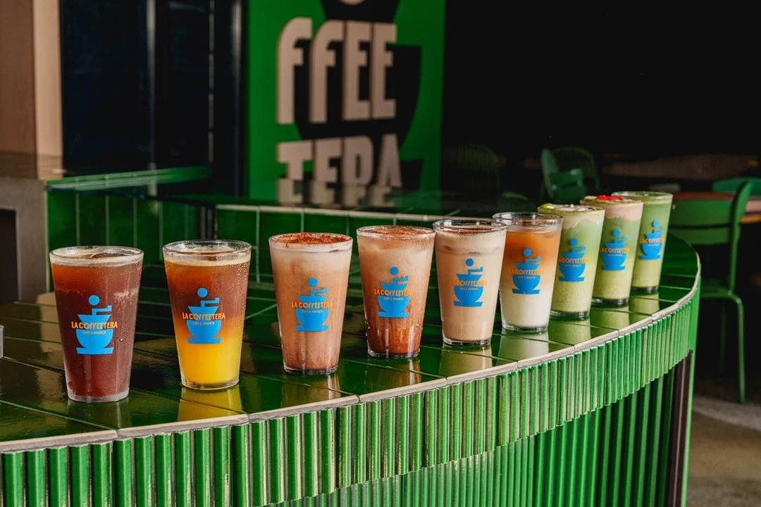 Varios vasos con bebidas diferentes en un mostrador verde en una cafetería.