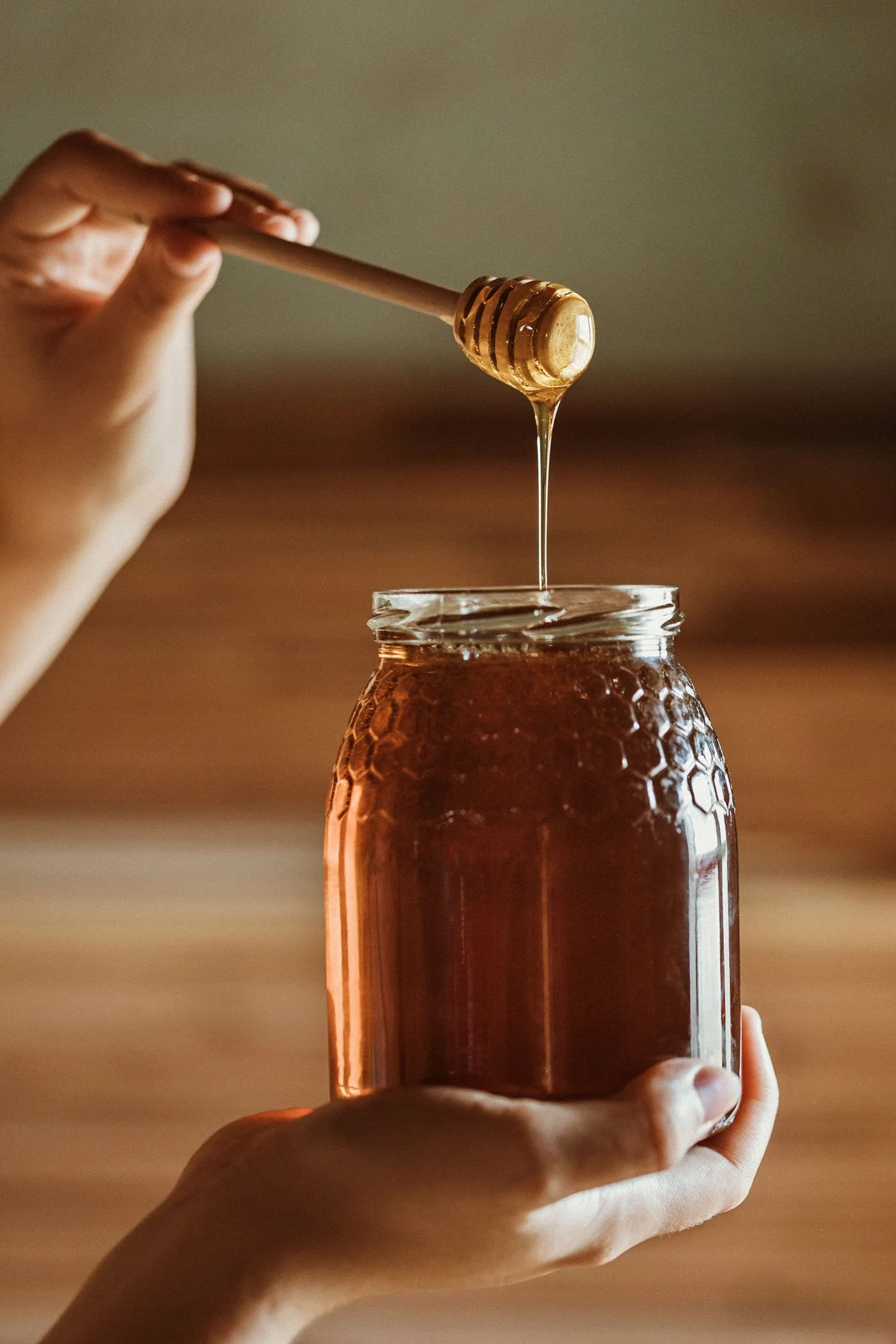 Persona poniendo miel en un frasco de cristal con un mango de madera.