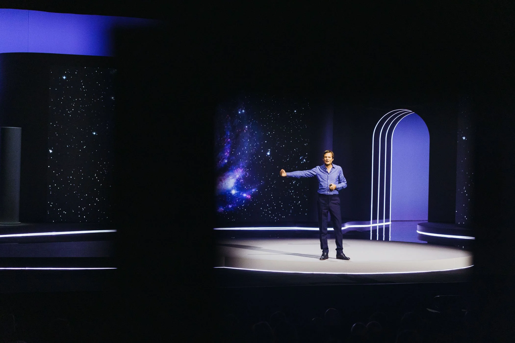 Persona dando una conferencia en un escenario con fondo de galaxia y luces blancas.