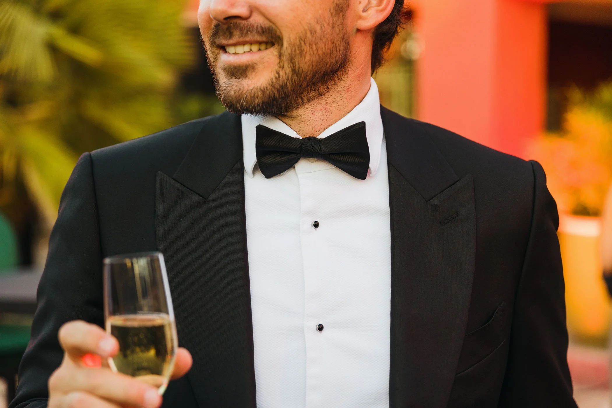 Hombre sonriendo vestido con esmoquin, sosteniendo una copa de champagne.