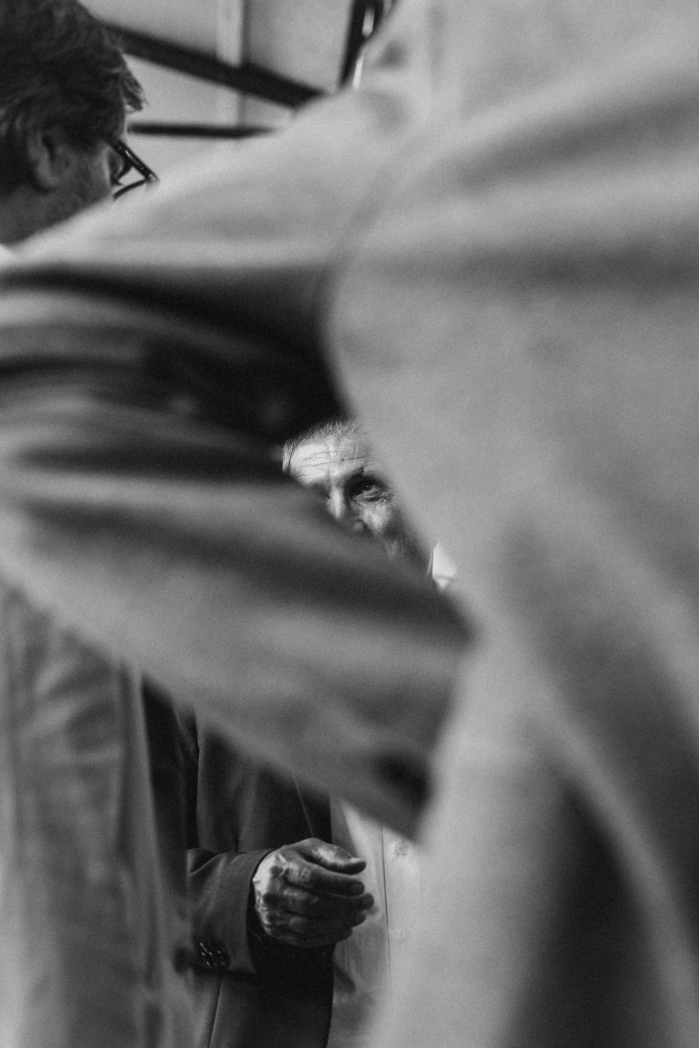 Una escena en blanco y negro que muestra a varias personas, una de ellas con expresión pensativa, parcialmente oculta por una hoja grande o planta en primer plano.