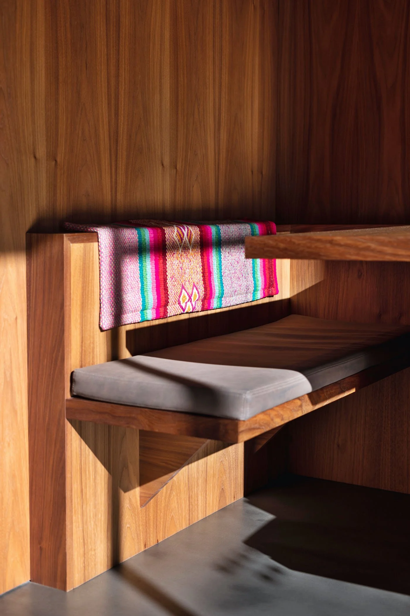 Banco de madera con cojín gris y manta colorida sobre respaldo
