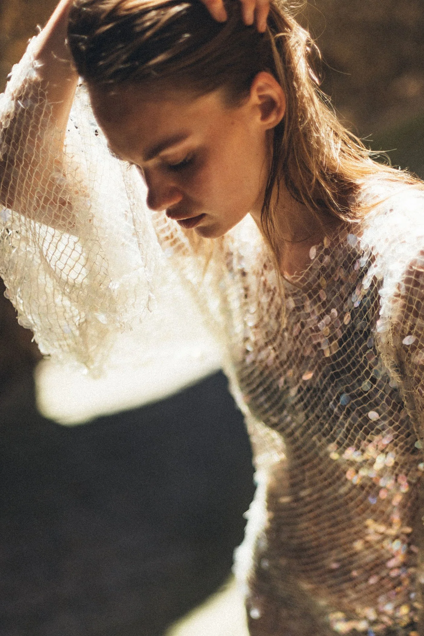 Mujer con cabello largo y ondulado, vestida con un vestido de lentejuelas, posando con la cabeza inclinada y la mano en la cabeza.