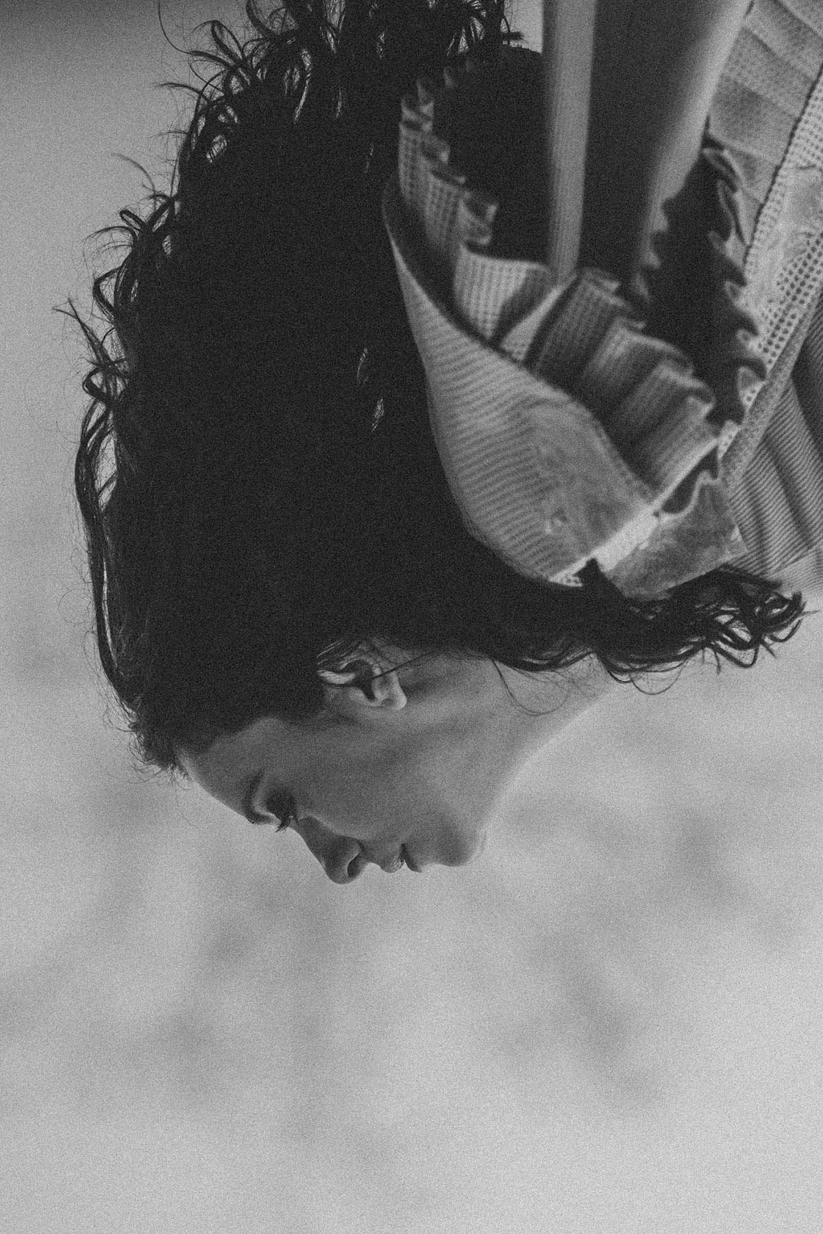 Retrato en negro y blanco de una mujer con cabello rizado, mirando hacia abajo, con un cojín con patrones en el fondo.