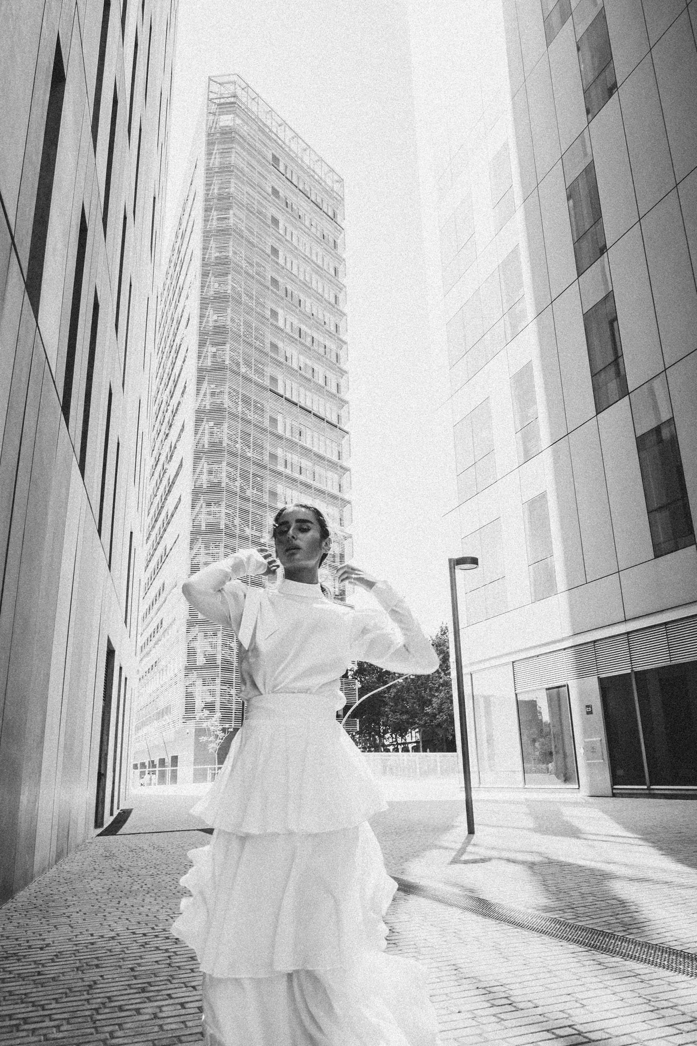 Mujer vestida con ropa blanca y falda larga en calle urbana moderna con edificios altos.