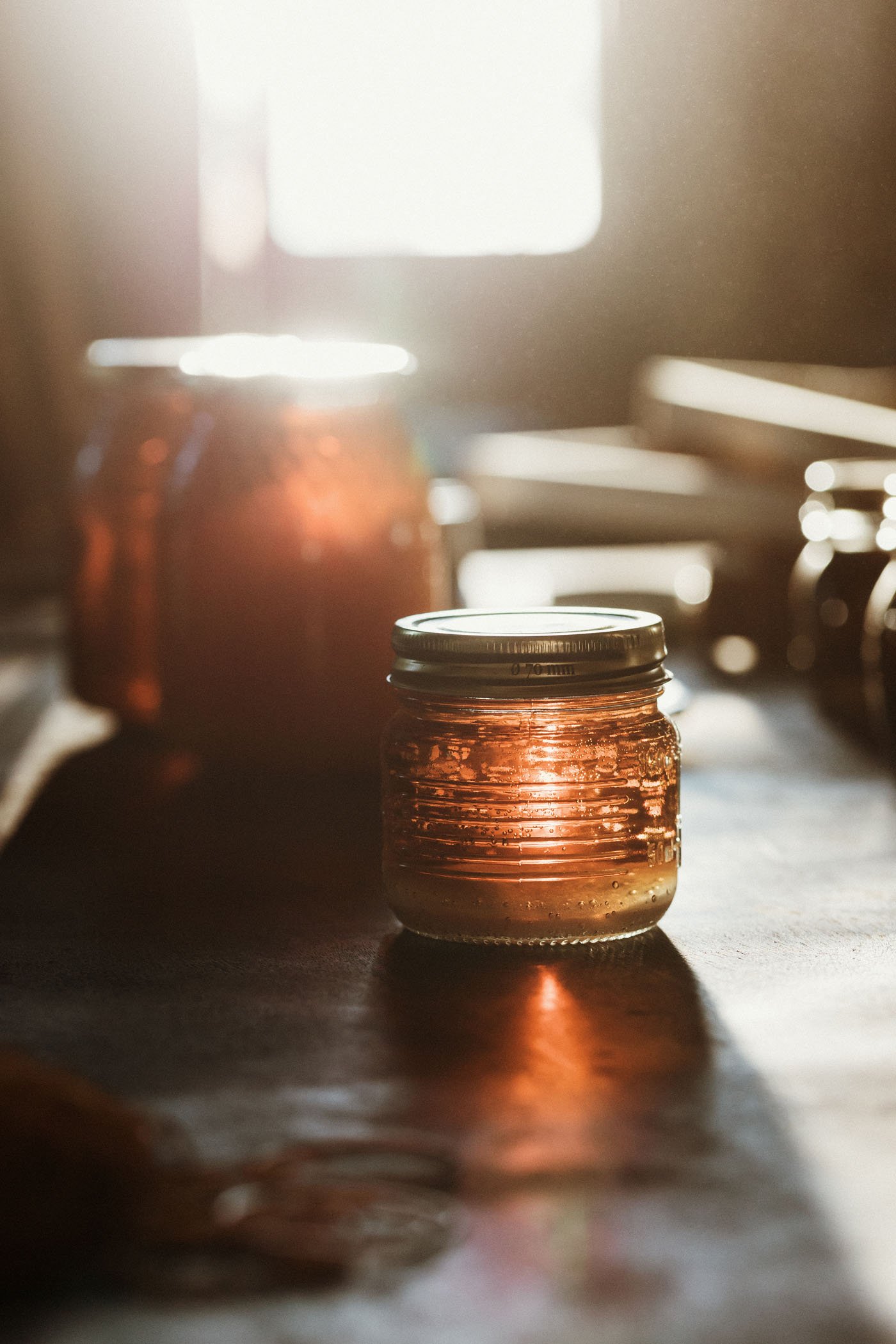 Frascos de conservas en una mesa con luz natural y sombras suaves.