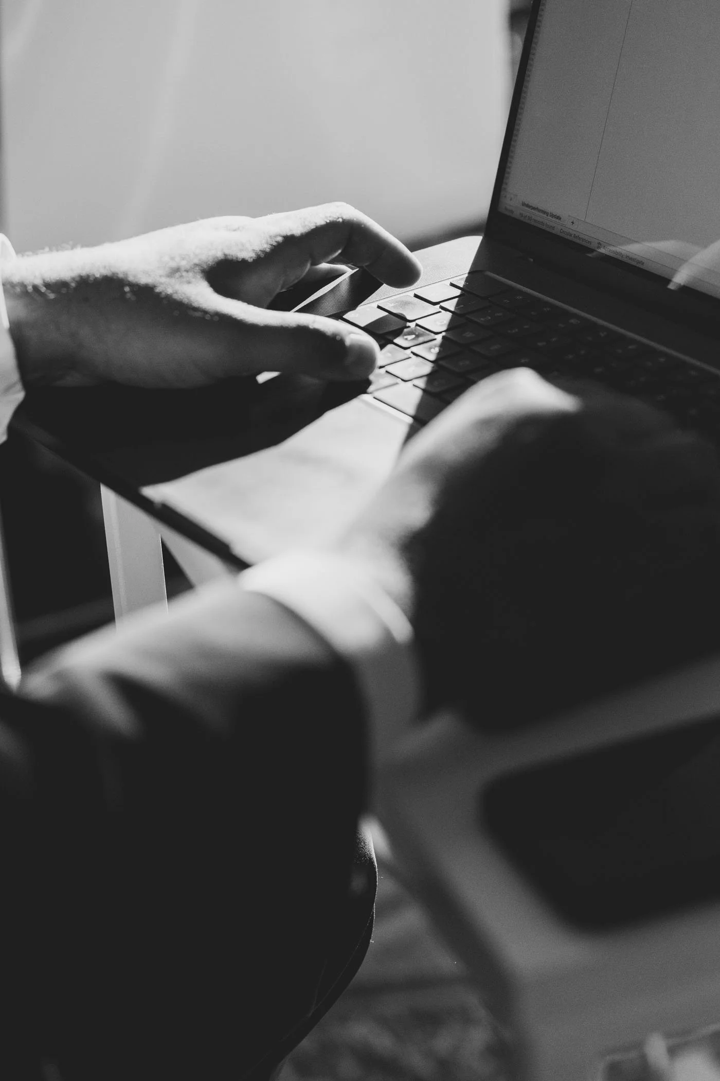 Hombre usando una laptop, en una mesa, en blanco y negro.