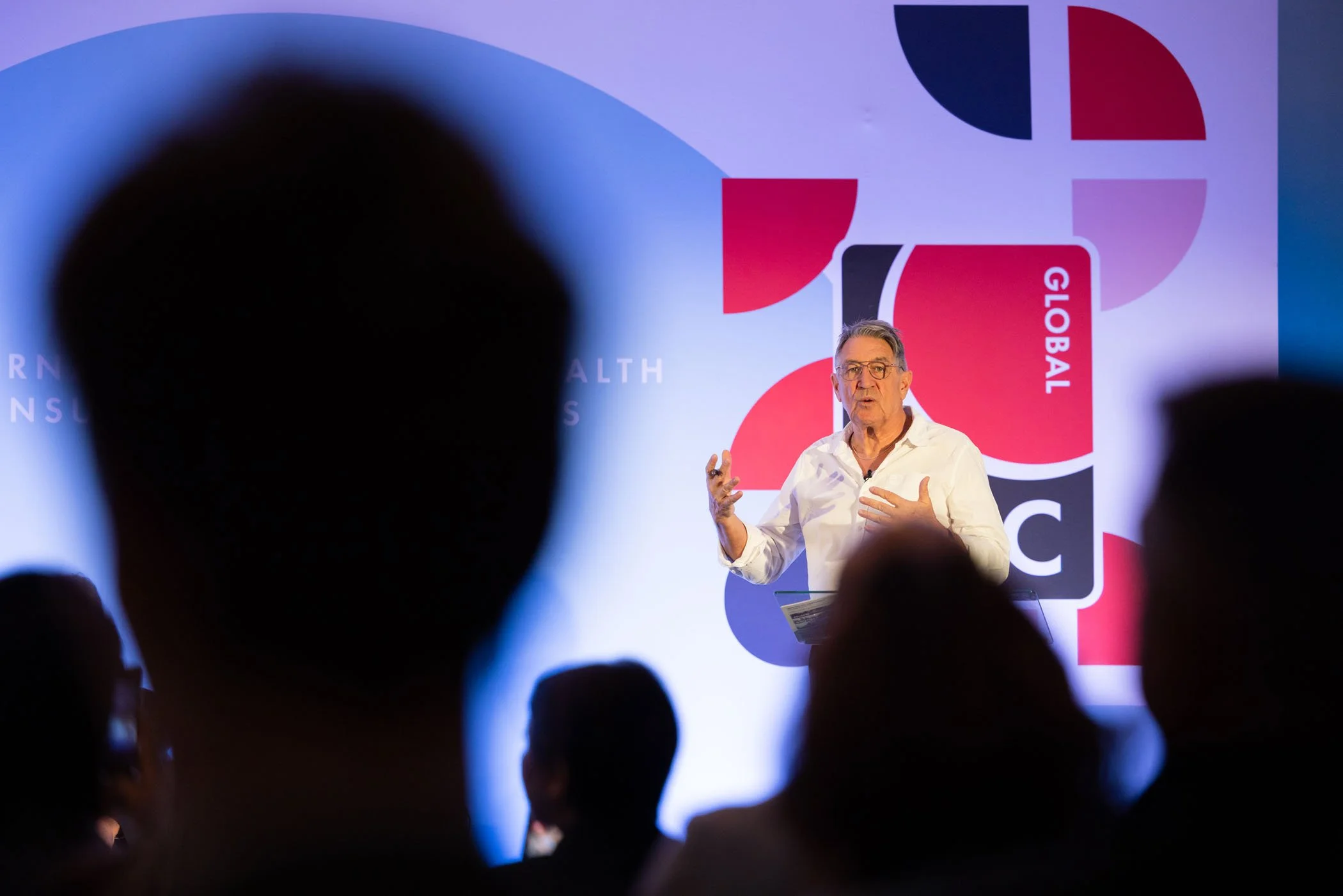 Hombre dando una conferencia frente a una pantalla con logotipos y texto en idioma inglés.