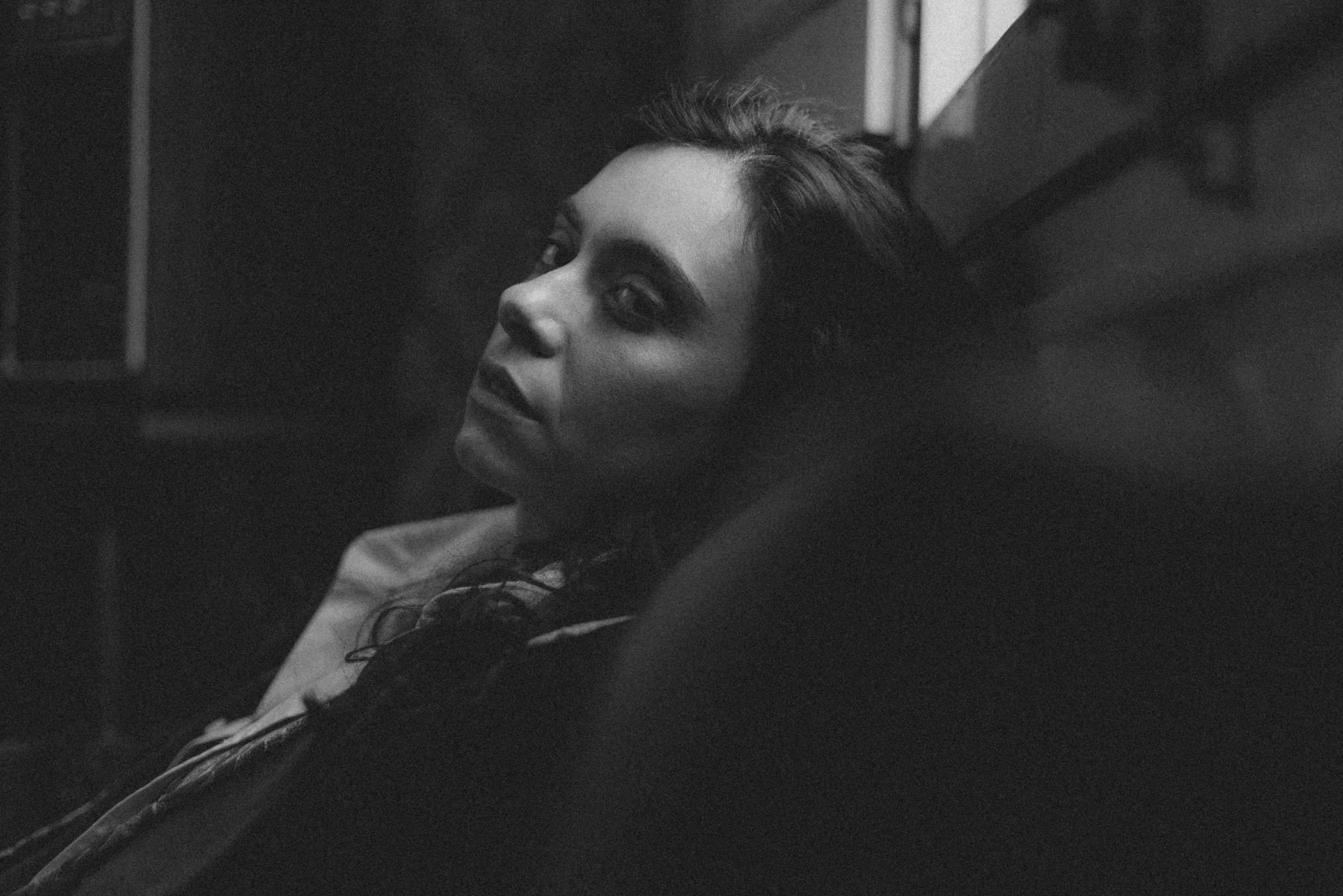 Mujer con expresión pensativa, en negro y blanco, mirando hacia la cámara, en un ambiente oscuro.