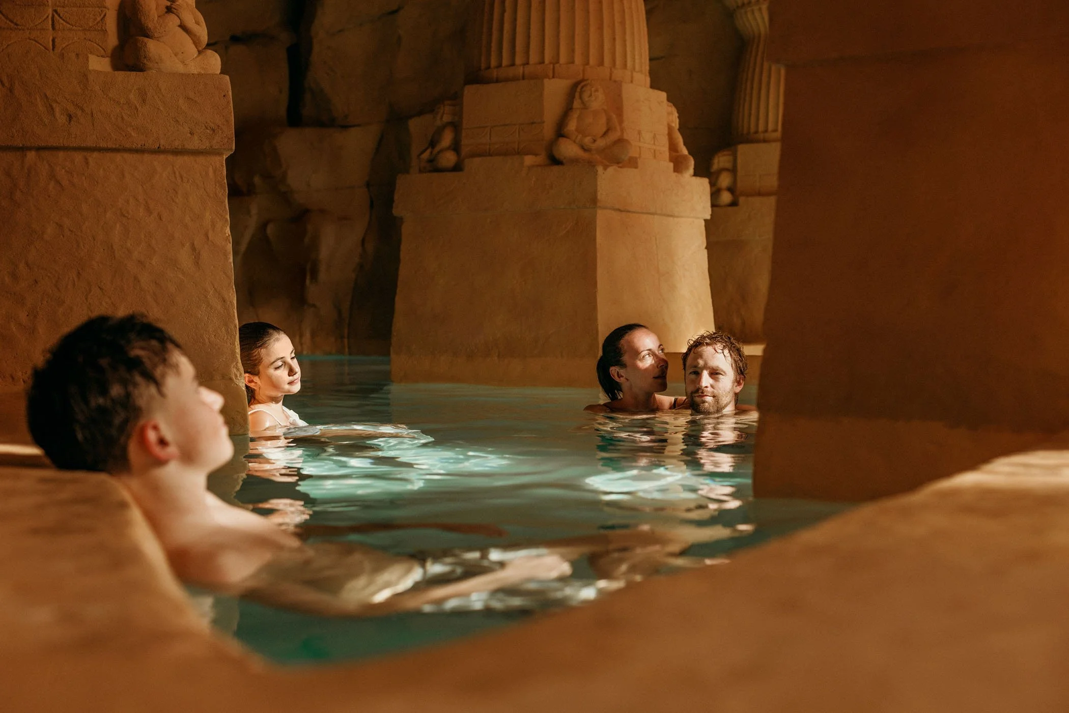 Personas disfrutando de una piscina en un ambiente inspirado en el antiguo Egipto con esculturas y columnas de piedra.