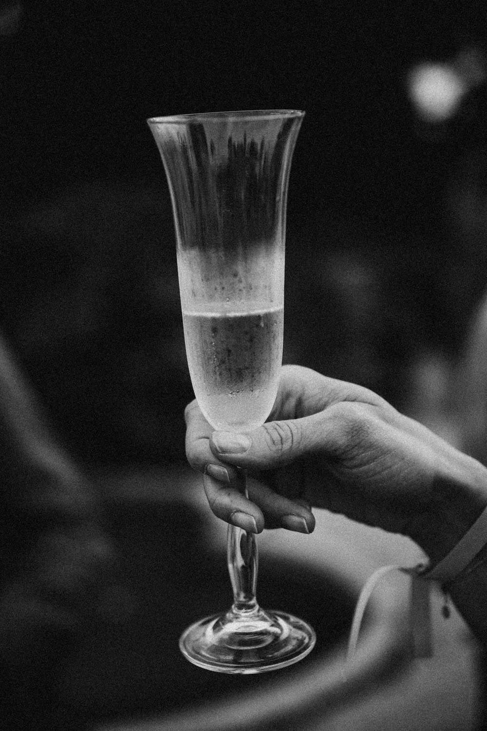 Una mano sostiene una copa de cristal con bebida espumosa, vista en blanco y negro.