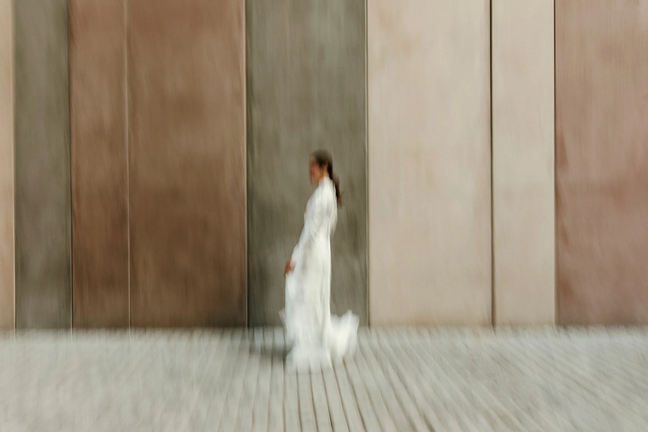 Mujer con vestido blanco caminando en un pasillo con paredes de diferentes colores.