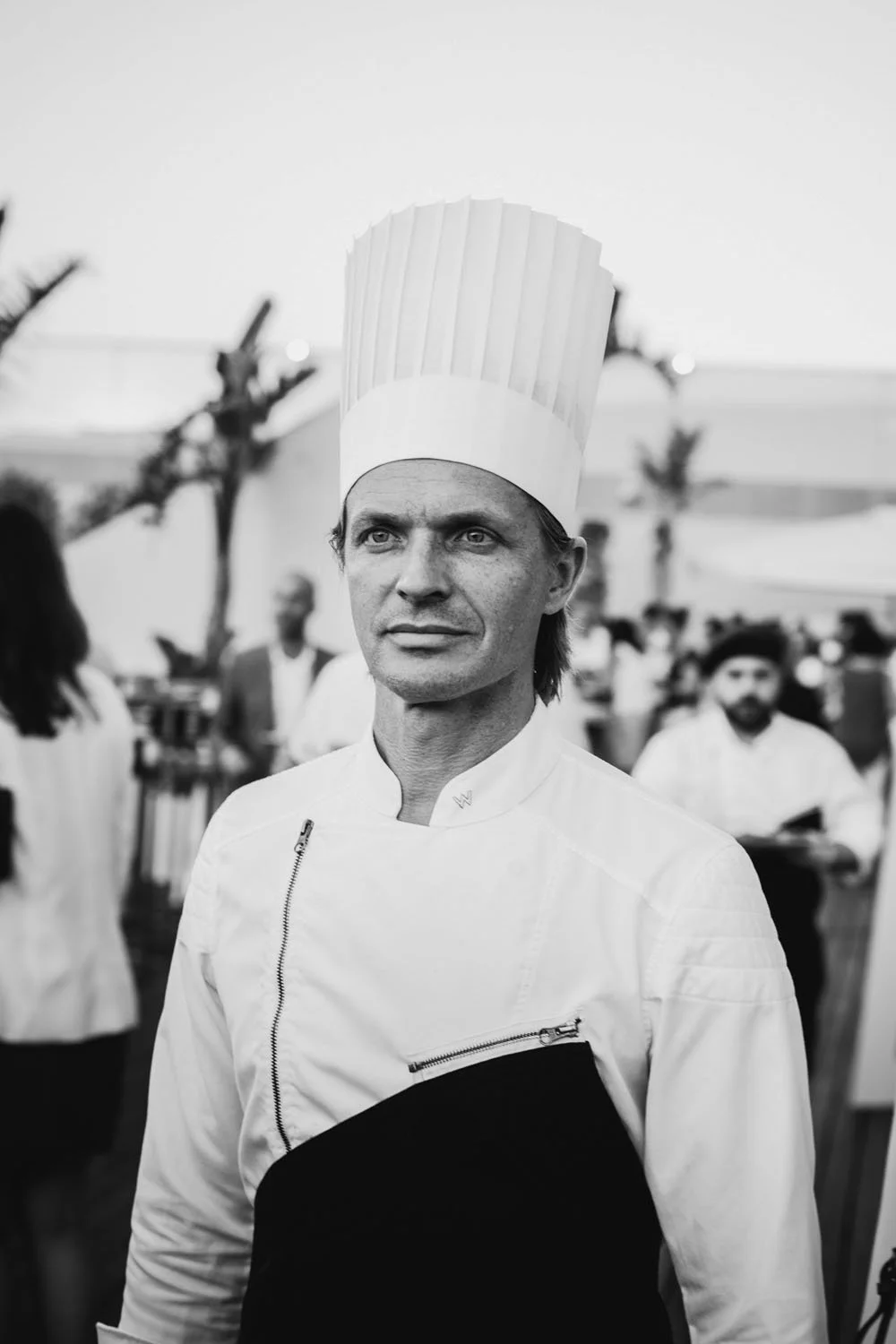 Chef con sombrero alto y chaqueta blanca en entorno de evento gastronómico.