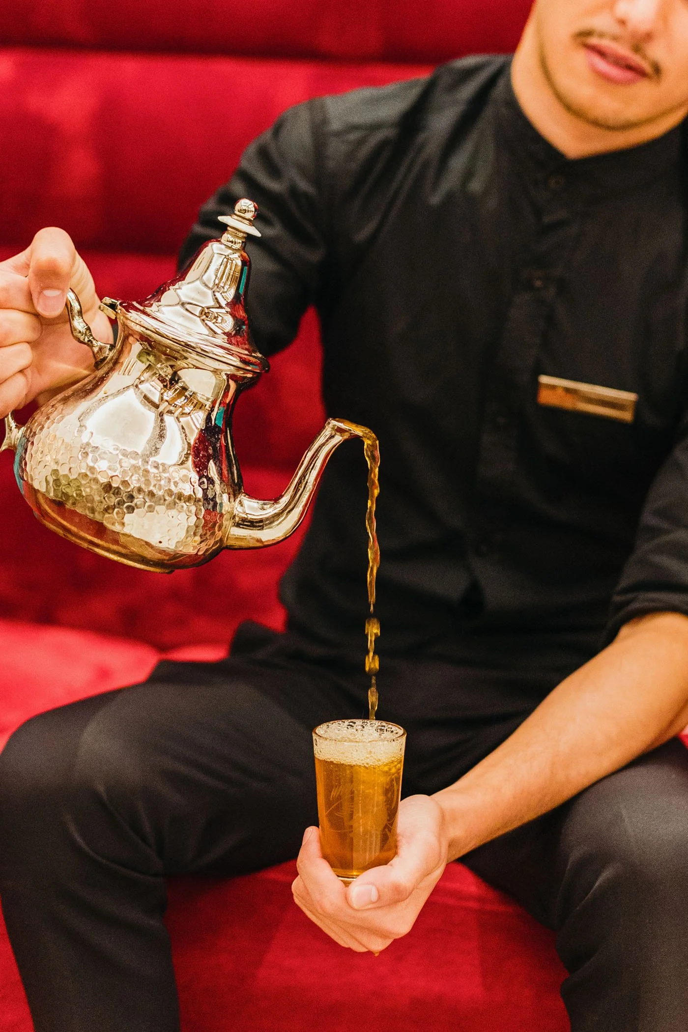 Hombre sirviendo té de una tetera dorada en un vaso en un restaurante.