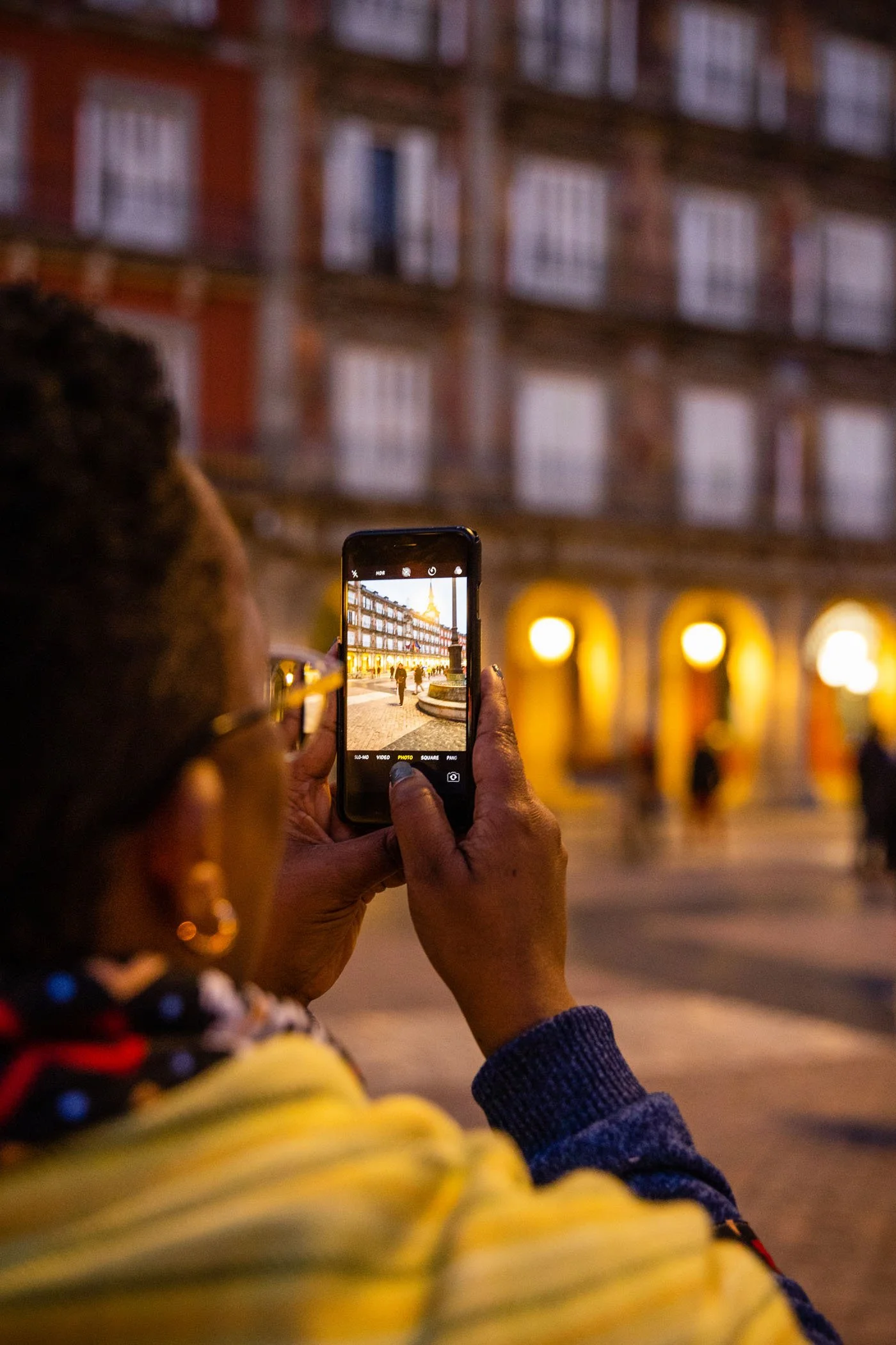 Persona tomando una foto de un edificio iluminado en la noche con su teléfono móvil.