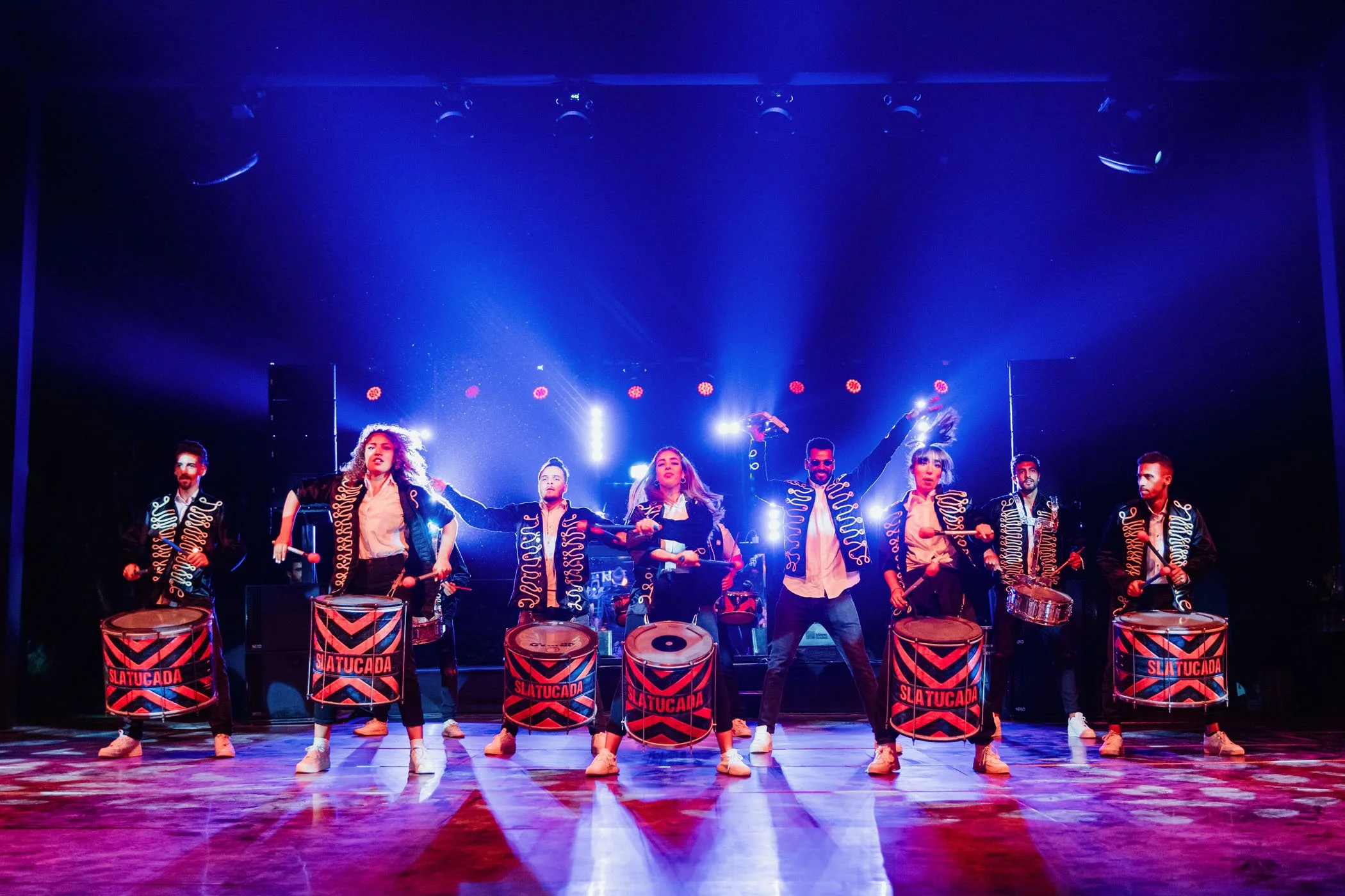 Grupo de músicos tocando tambores en un escenario con luces brillantes.