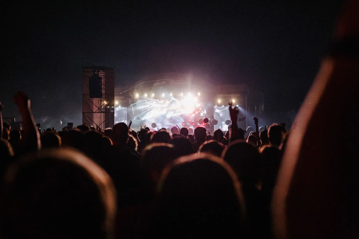 Concierto nocturno con multitud de personas bailando y disfrutando, escenario con luces brillantes y pantallas grandes.