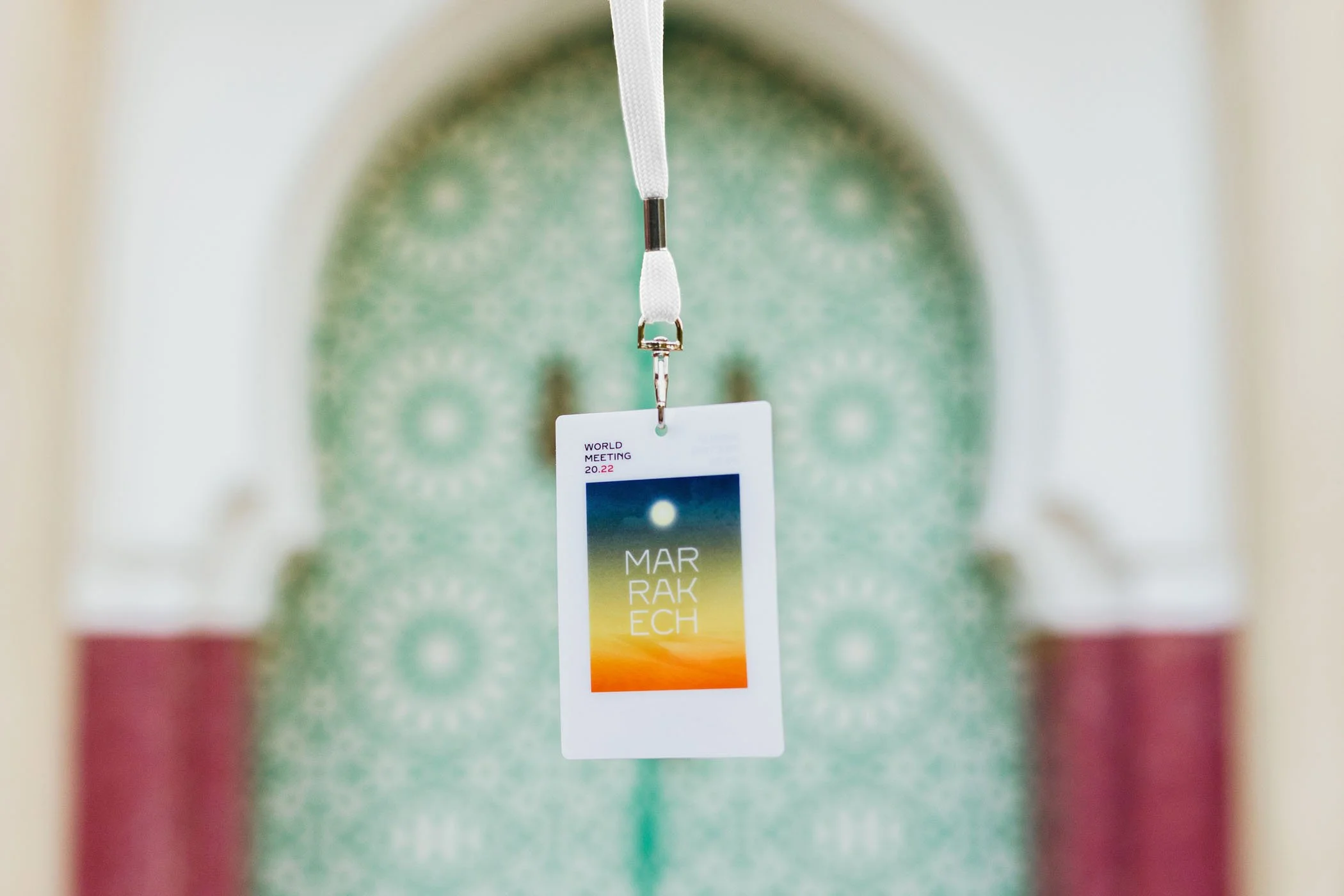 Tarjeta de identificación en un cordón con fondo borroso de la entrada a un edificio con arco decorado con mosaicos verdes y blancos.