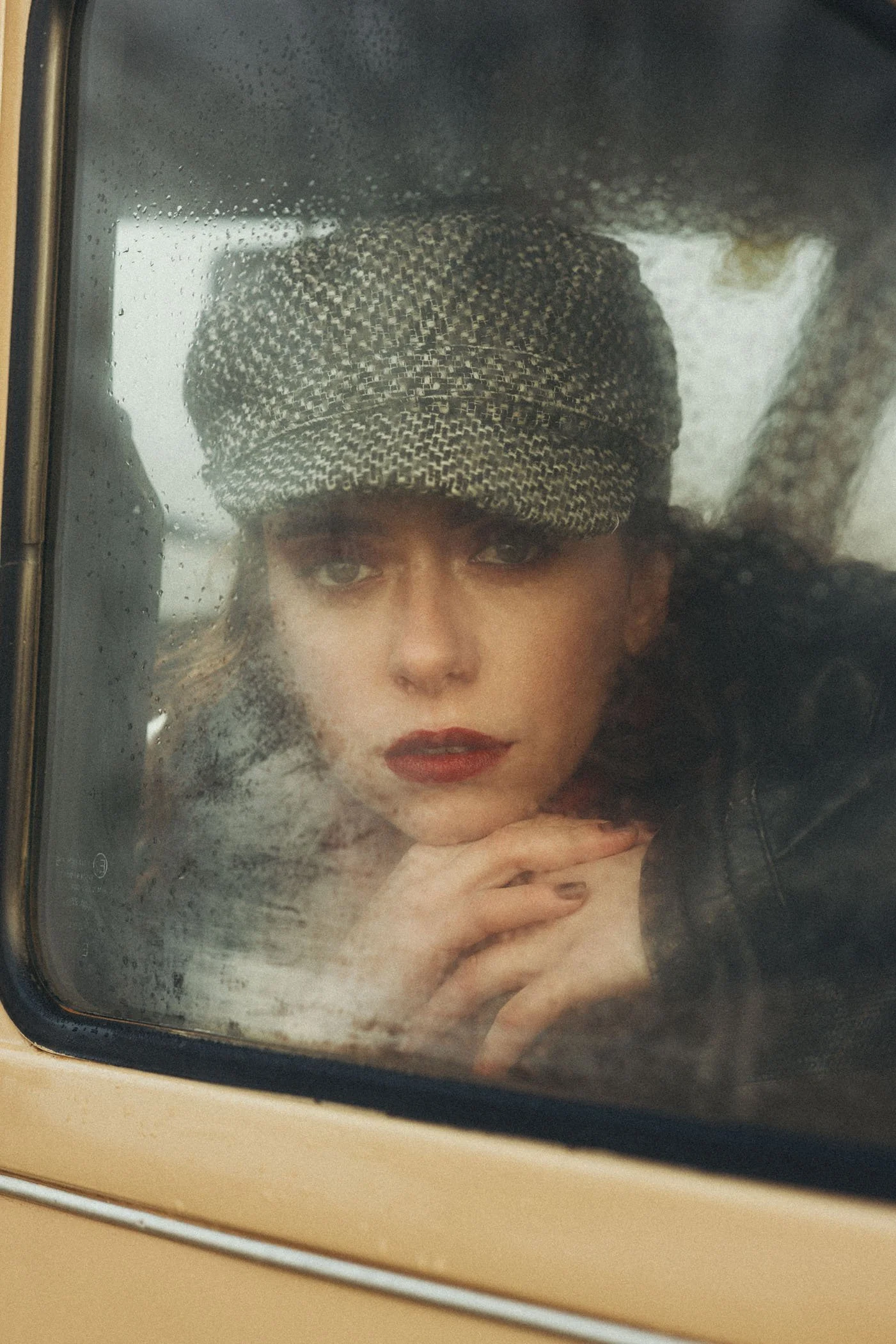 Mujer con gorra de estampado de cuadros mirando por la ventana con lluvia