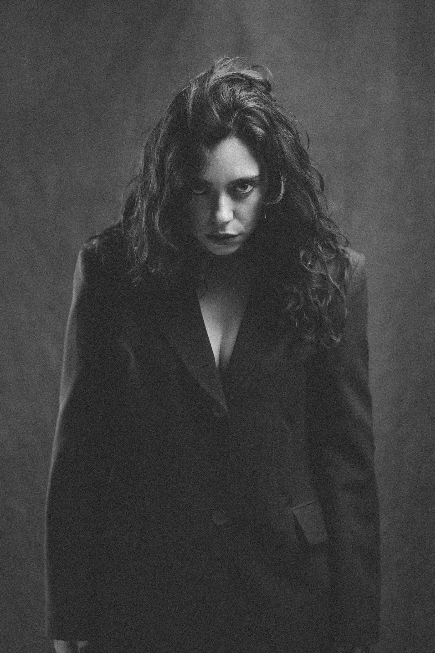 Retrato en blanco y negro de una mujer con cabello rizado y expresión intensa, vistiendo una chaqueta negra.